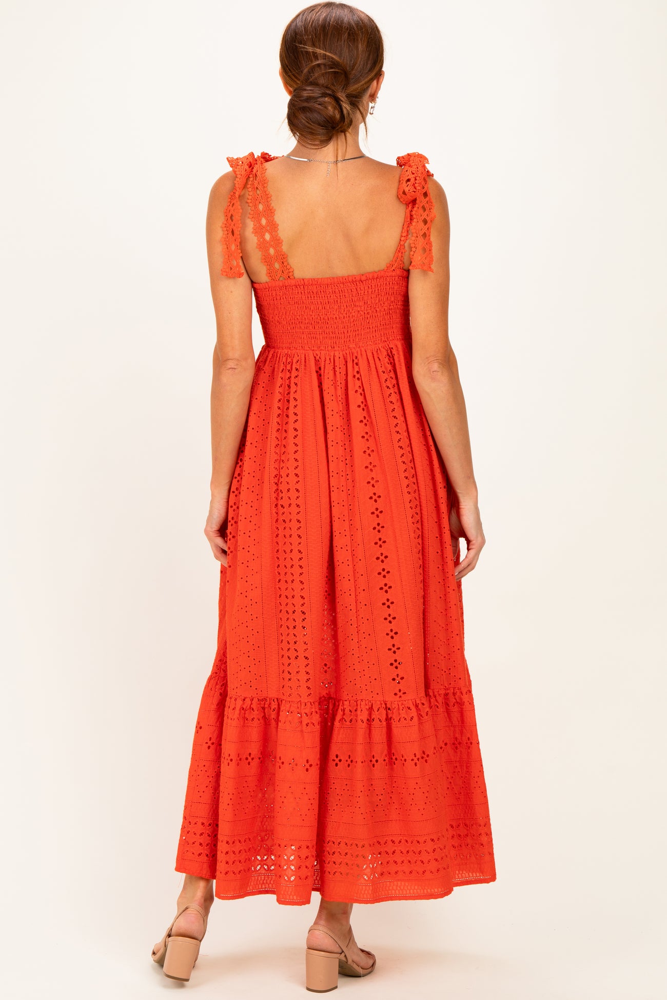 woman wearing an orange maxi dress with shoulder ties and lace detailing, seen from the back