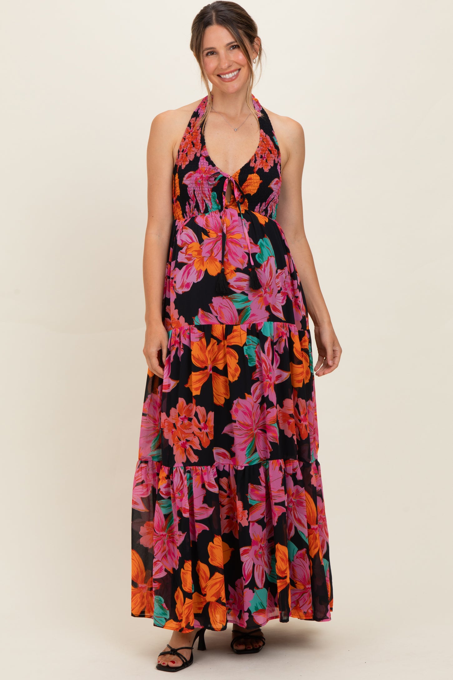 woman wearing a black maternity maxi dress with vibrant floral patterns and a halter neckline, showcasing her baby bump