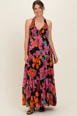 woman wearing a black maternity maxi dress with vibrant floral patterns and a halter neckline, showcasing her baby bump