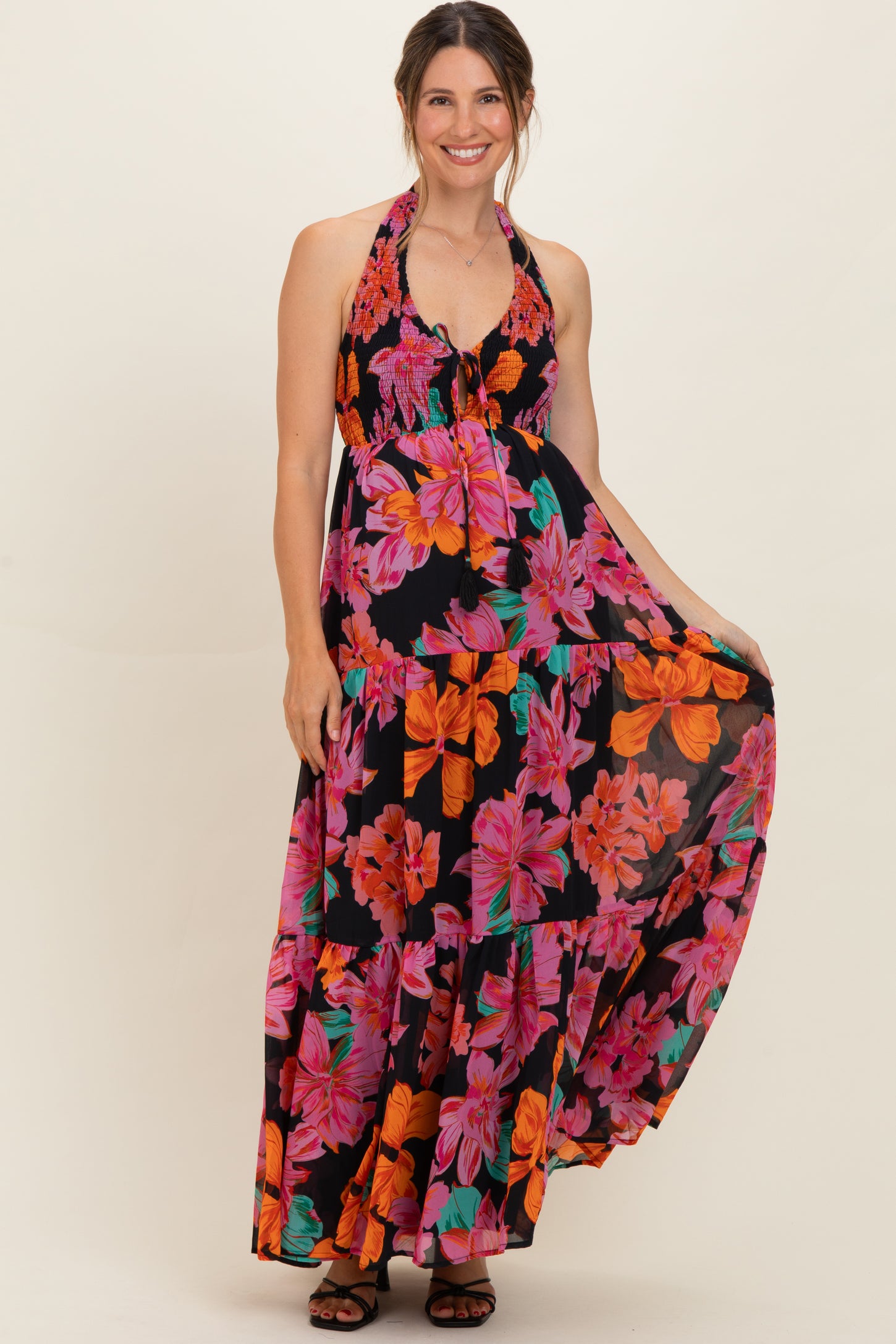 woman wearing a black maternity halter maxi dress with vibrant pink and orange floral print, holding her baby bump