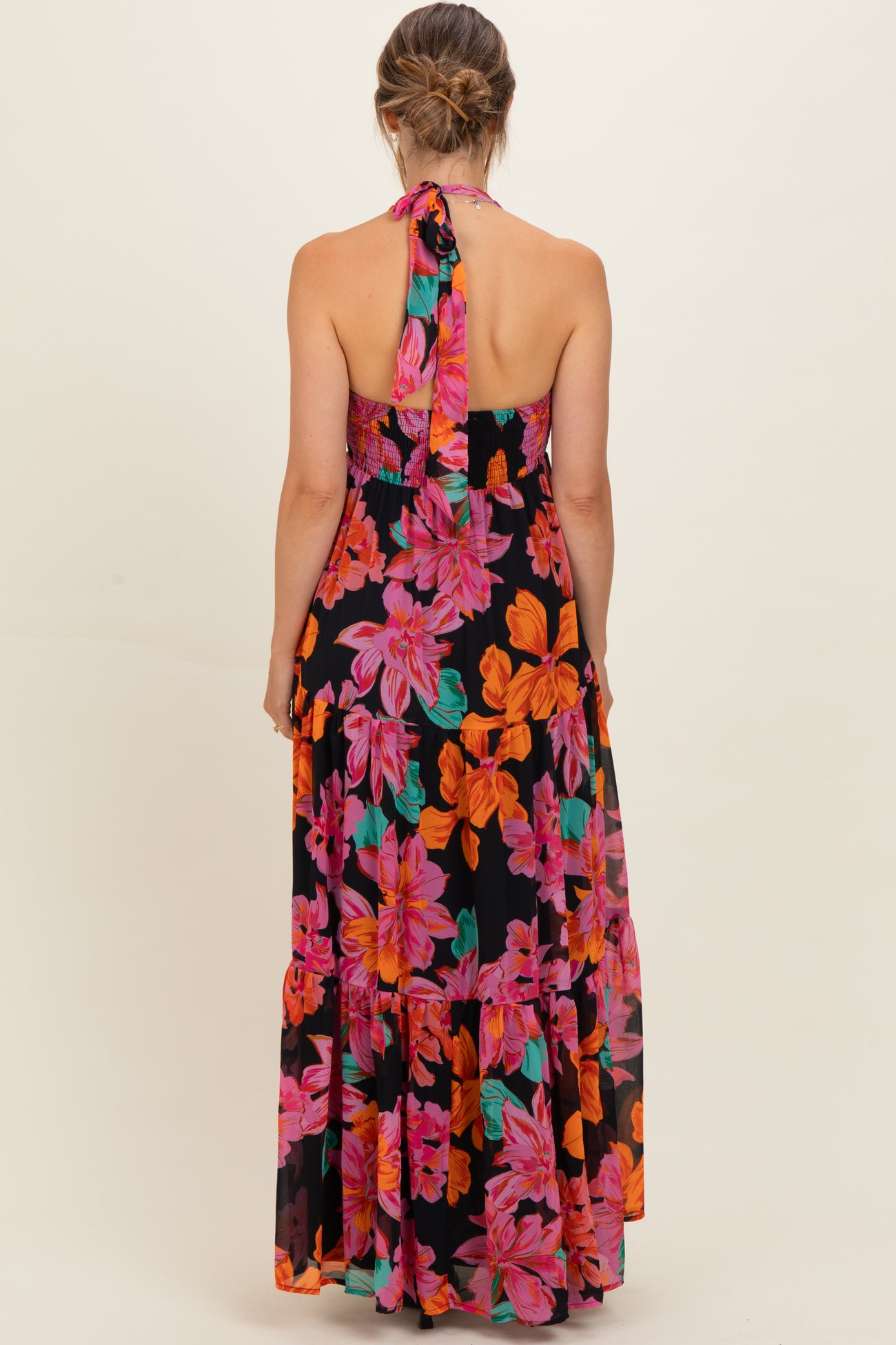 woman wearing a black floral halter maternity maxi dress with vibrant pink and orange flowers