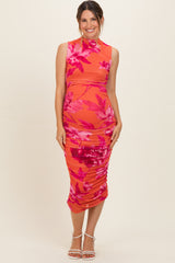 woman wearing a coral floral maternity dress with ruching and a high neckline, showcasing her baby bump