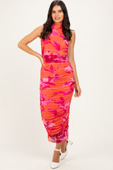 woman wearing a sleeveless floral midi dress in shades of pink and orange with ruching details and a fitted silhouette