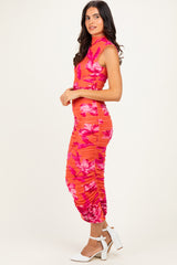woman wearing a vibrant coral floral midi dress with ruching and a high neckline, standing in profile