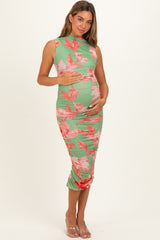 woman wearing a floral green maternity dress with ruched details, holding her baby bump