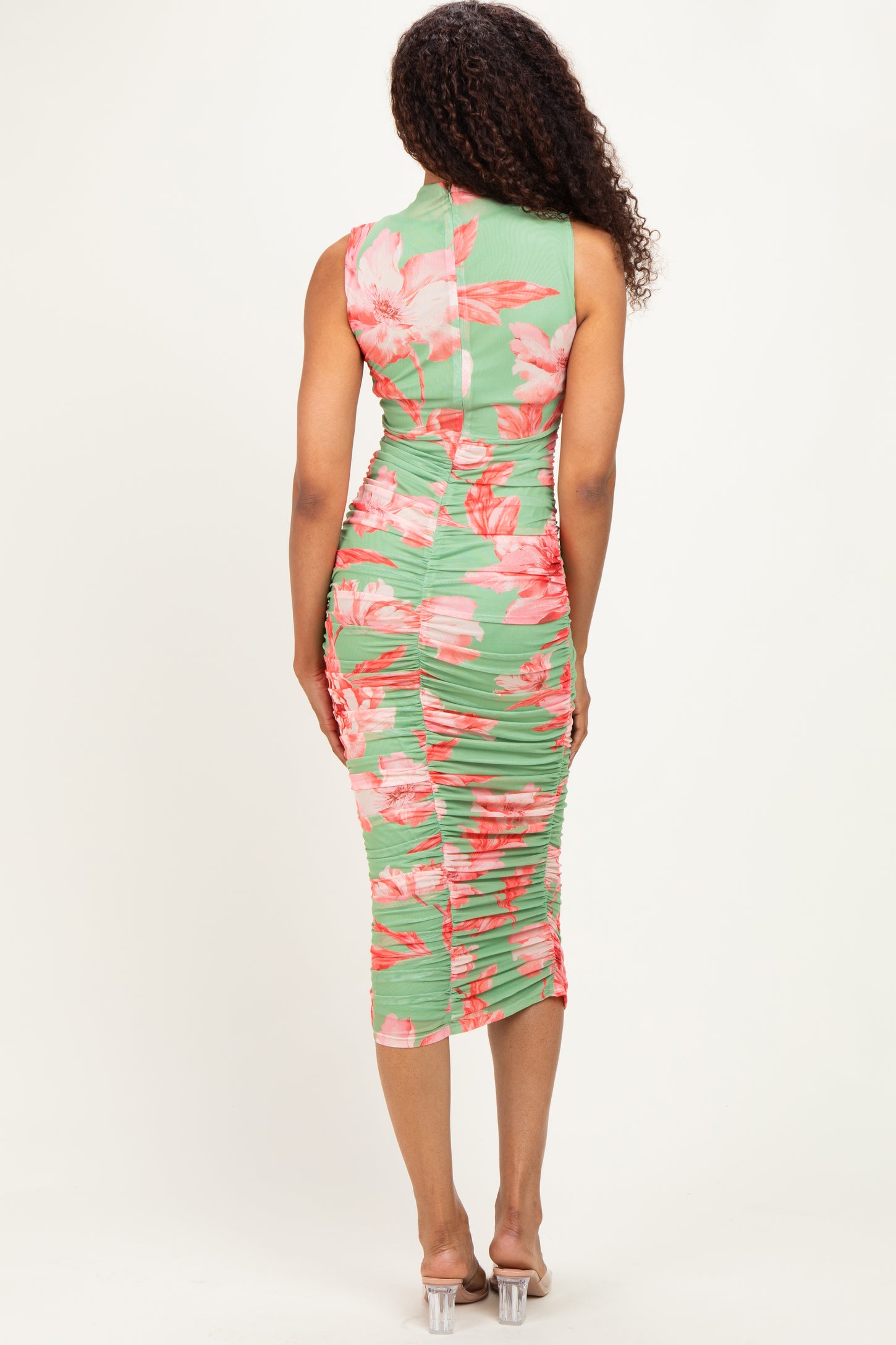 woman wearing a green floral bodycon dress with ruching detailing and a mid-length hemline, seen from the back