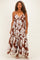 woman wearing a brown floral maxi dress with spaghetti straps and a tiered skirt, styled with curls and heels