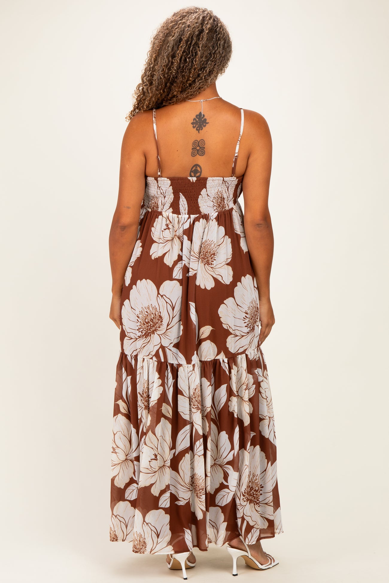 woman wearing a brown floral maxi dress with a smocked bodice and spaghetti straps, showing the back view