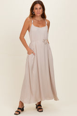 woman wearing a beige maxi dress with adjustable straps and a tied waist, featuring side pockets