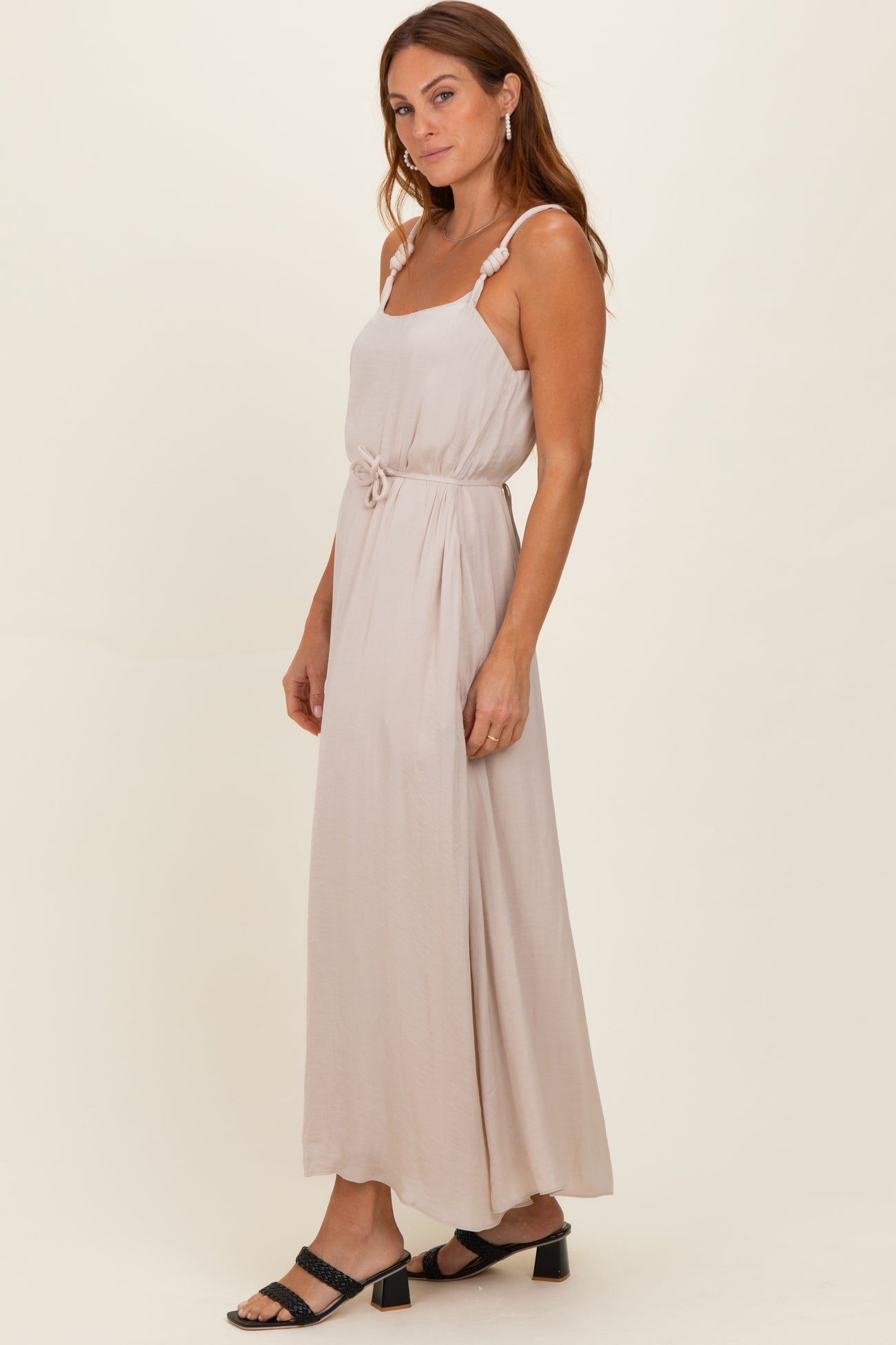 woman wearing a light beige sleeveless maxi dress with a waist tie and ruffled straps