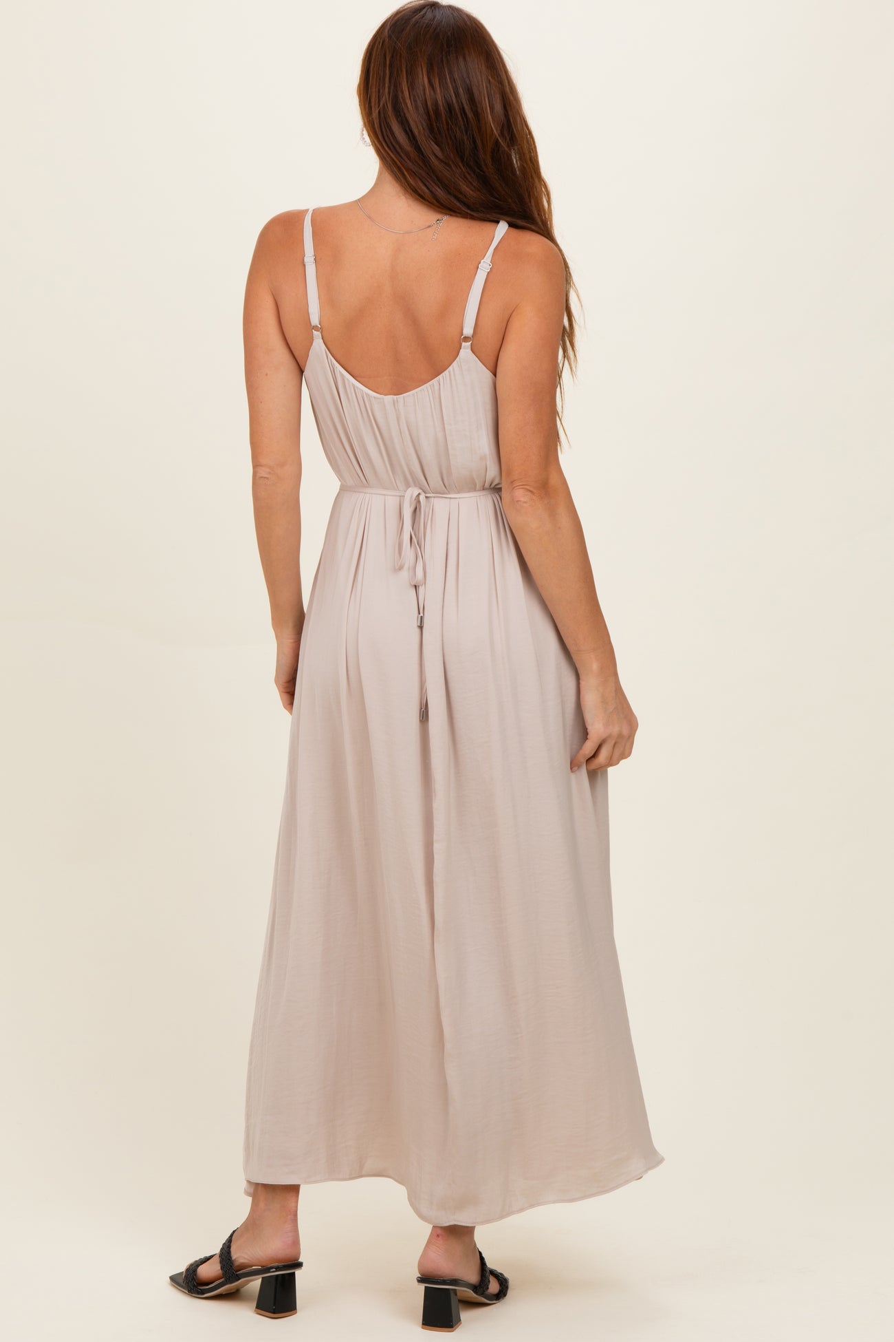 woman wearing a back view of a light beige maxi dress with adjustable straps and a tie waist detail