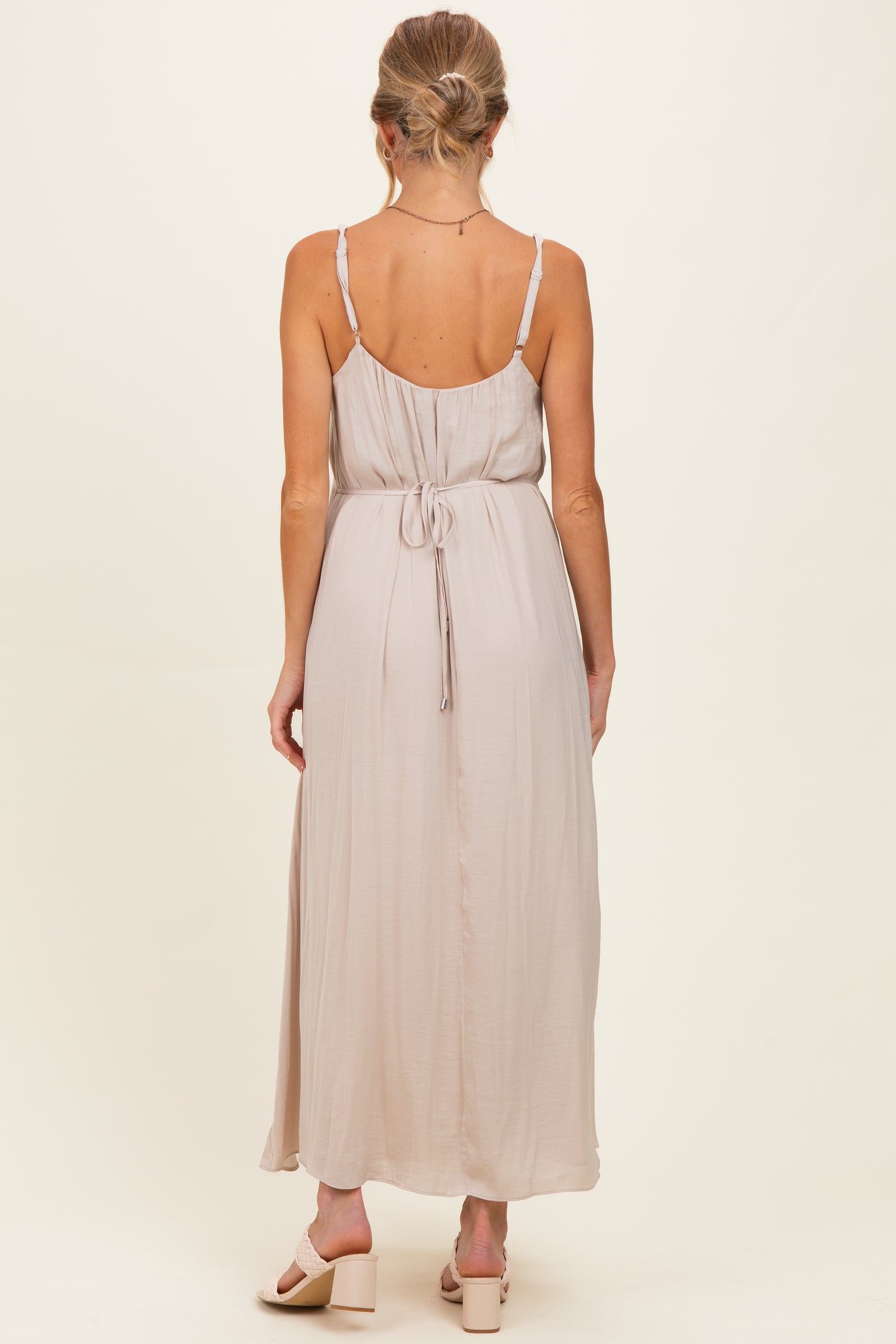 woman wearing a light taupe spaghetti strap maxi maternity dress with a tie-back detail