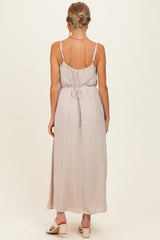woman wearing a light taupe spaghetti strap maxi maternity dress with a tie-back detail