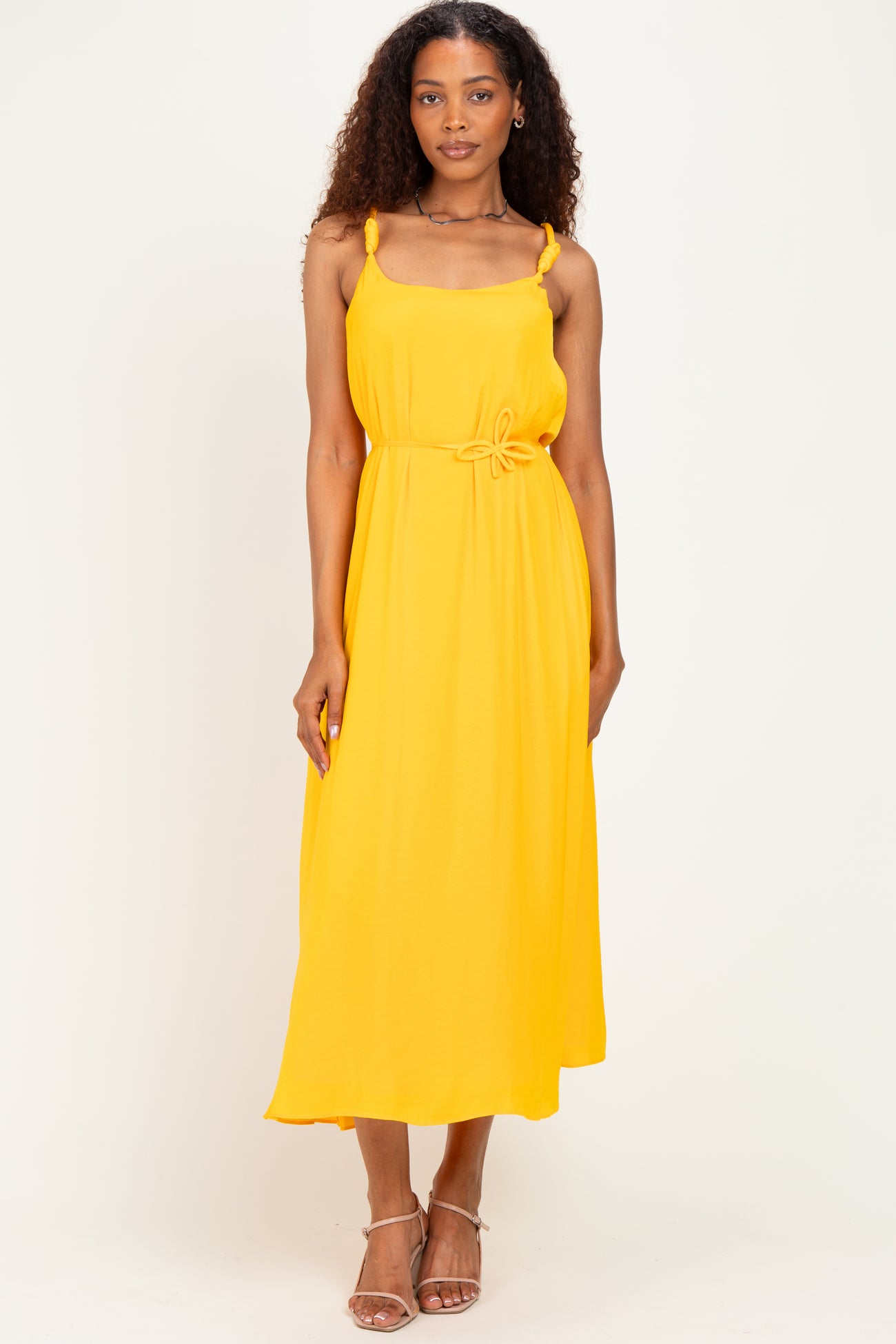 woman wearing a sleeveless yellow maxi dress with knot detail at the waist and delicate straps