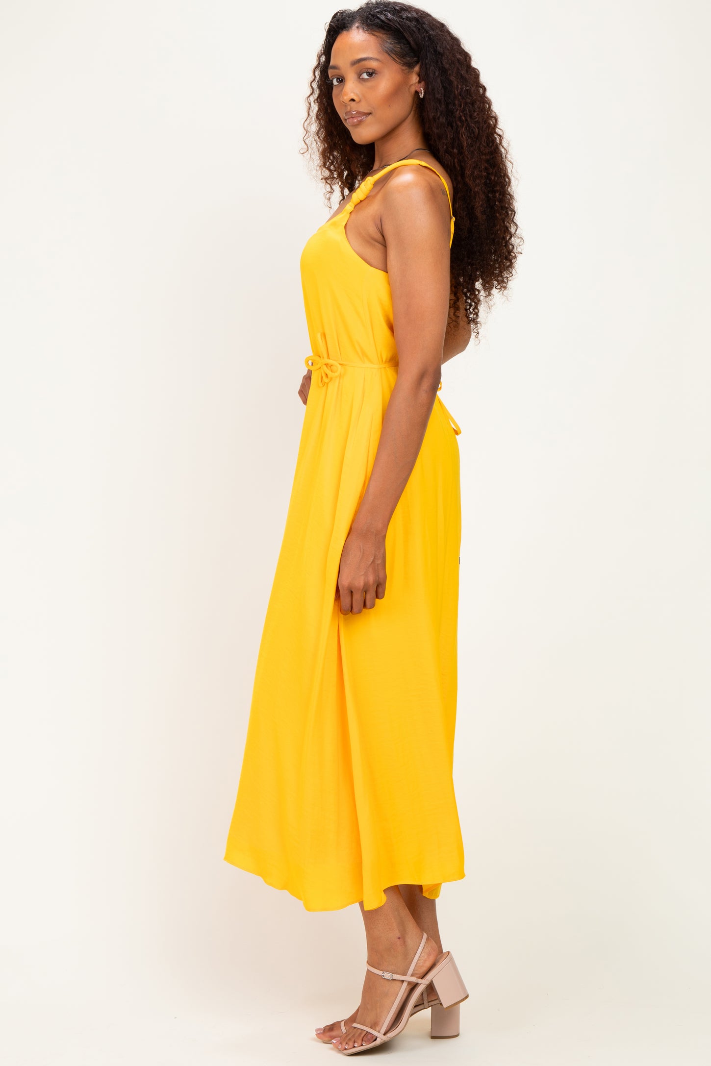woman wearing a yellow sleeveless maxi dress with a tie waist detail and curly hair