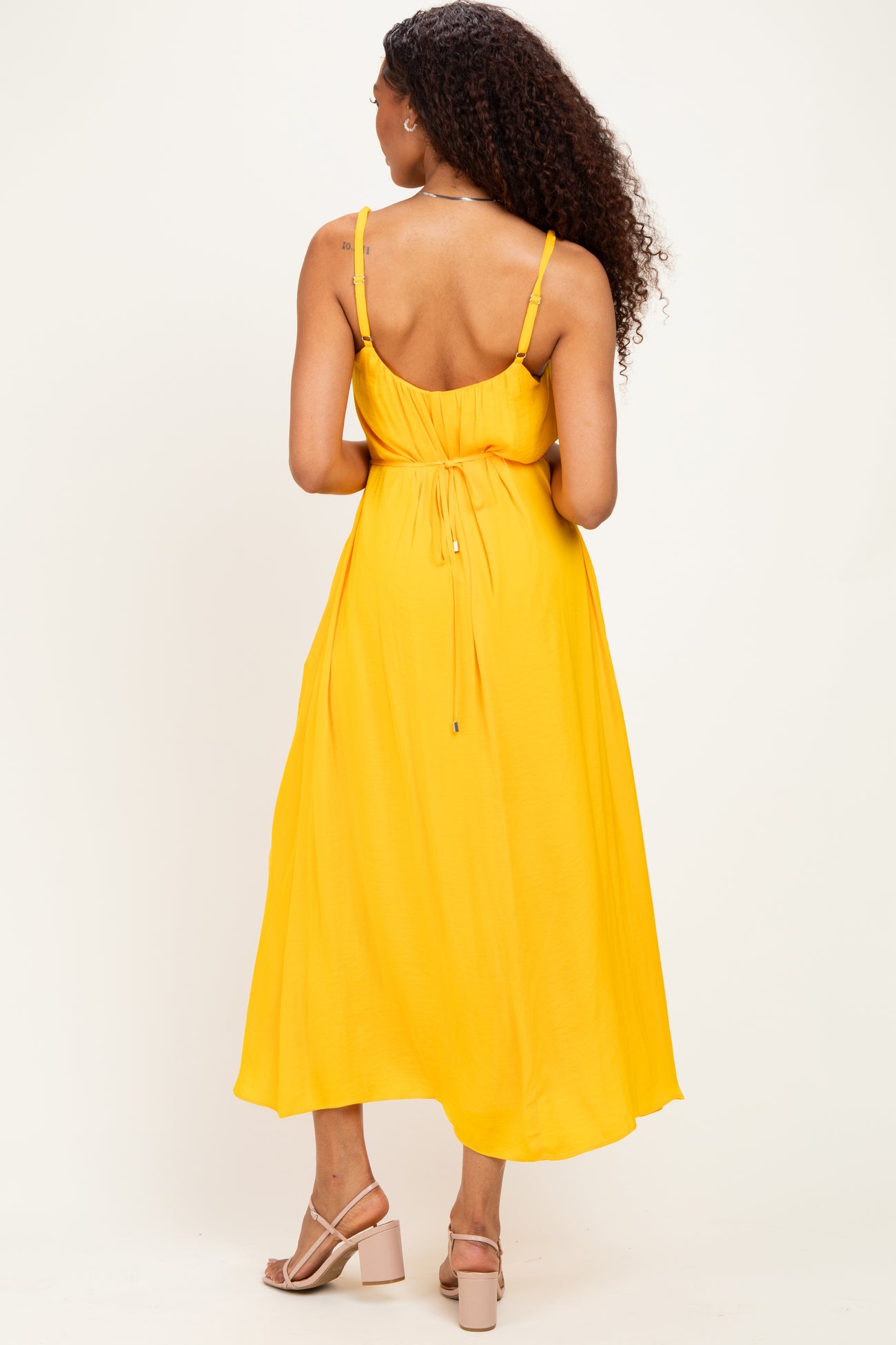 woman wearing a yellow backless maxi dress with a tie waist and spaghetti straps