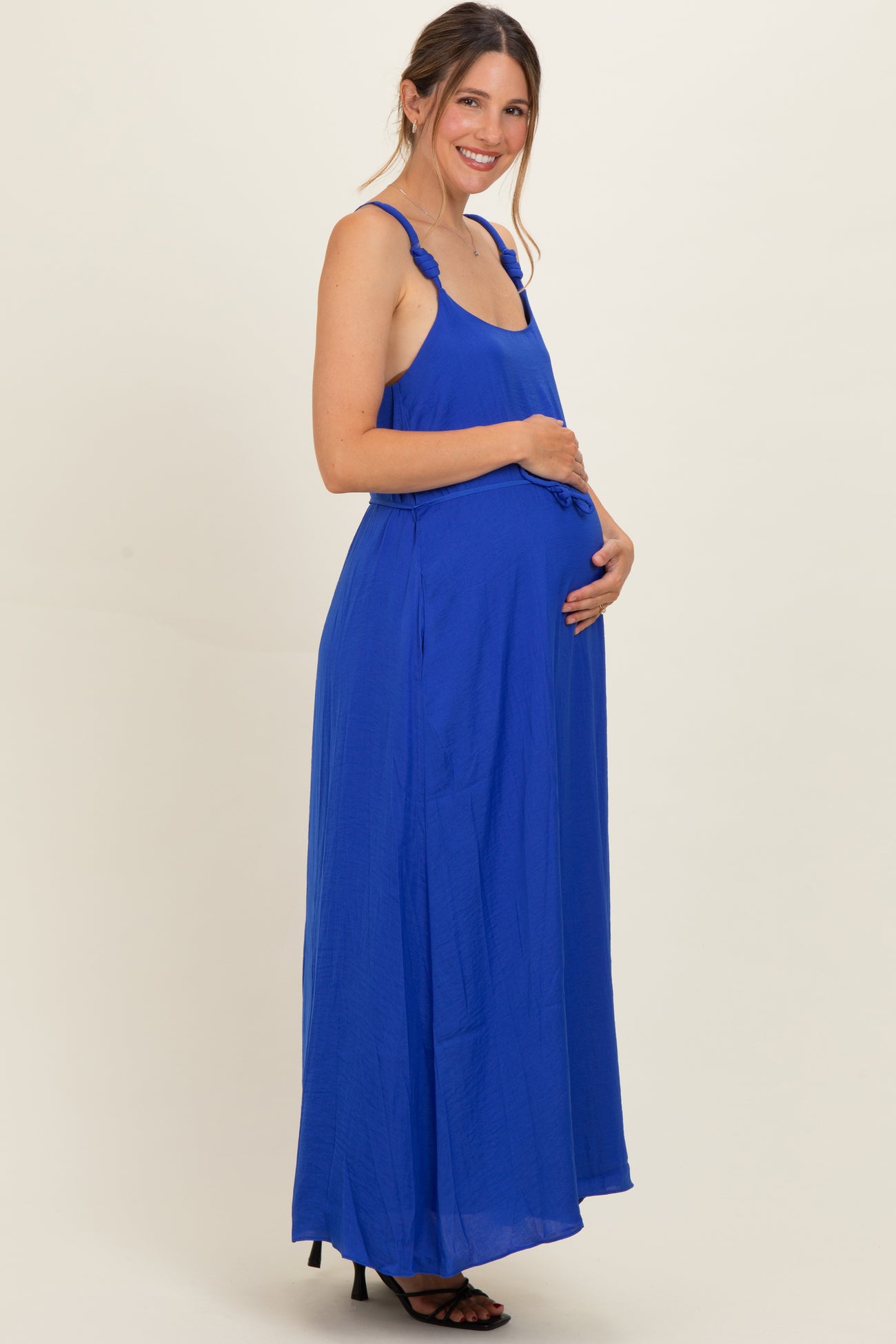 woman wearing a bright blue maternity maxi dress, cradling her baby bump