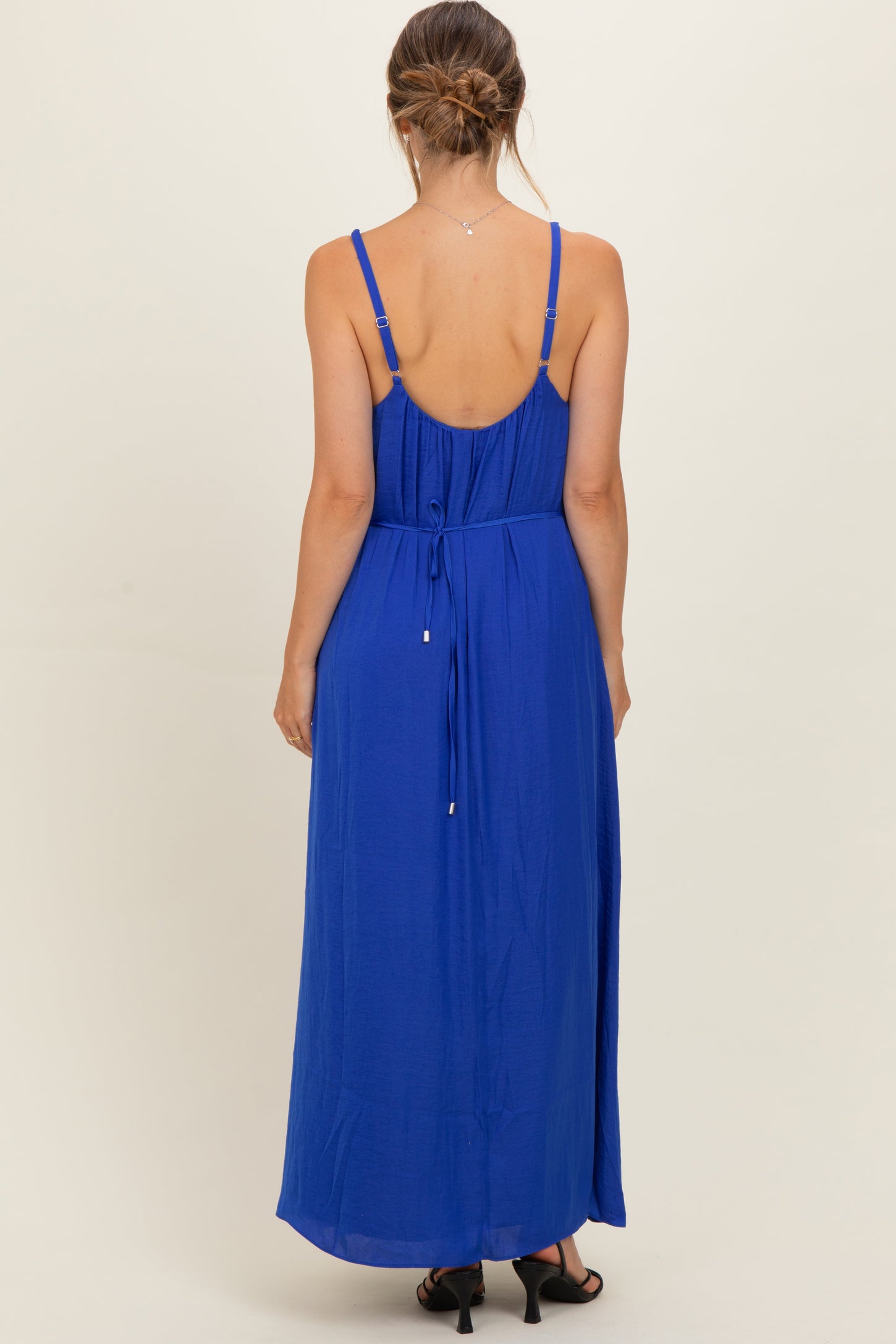 woman wearing a backless bright blue maternity maxi dress with adjustable straps and a tied waist detail