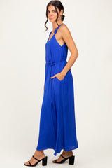 woman wearing a sleeveless royal blue maxi dress with a tie waist and side pockets, standing sideways