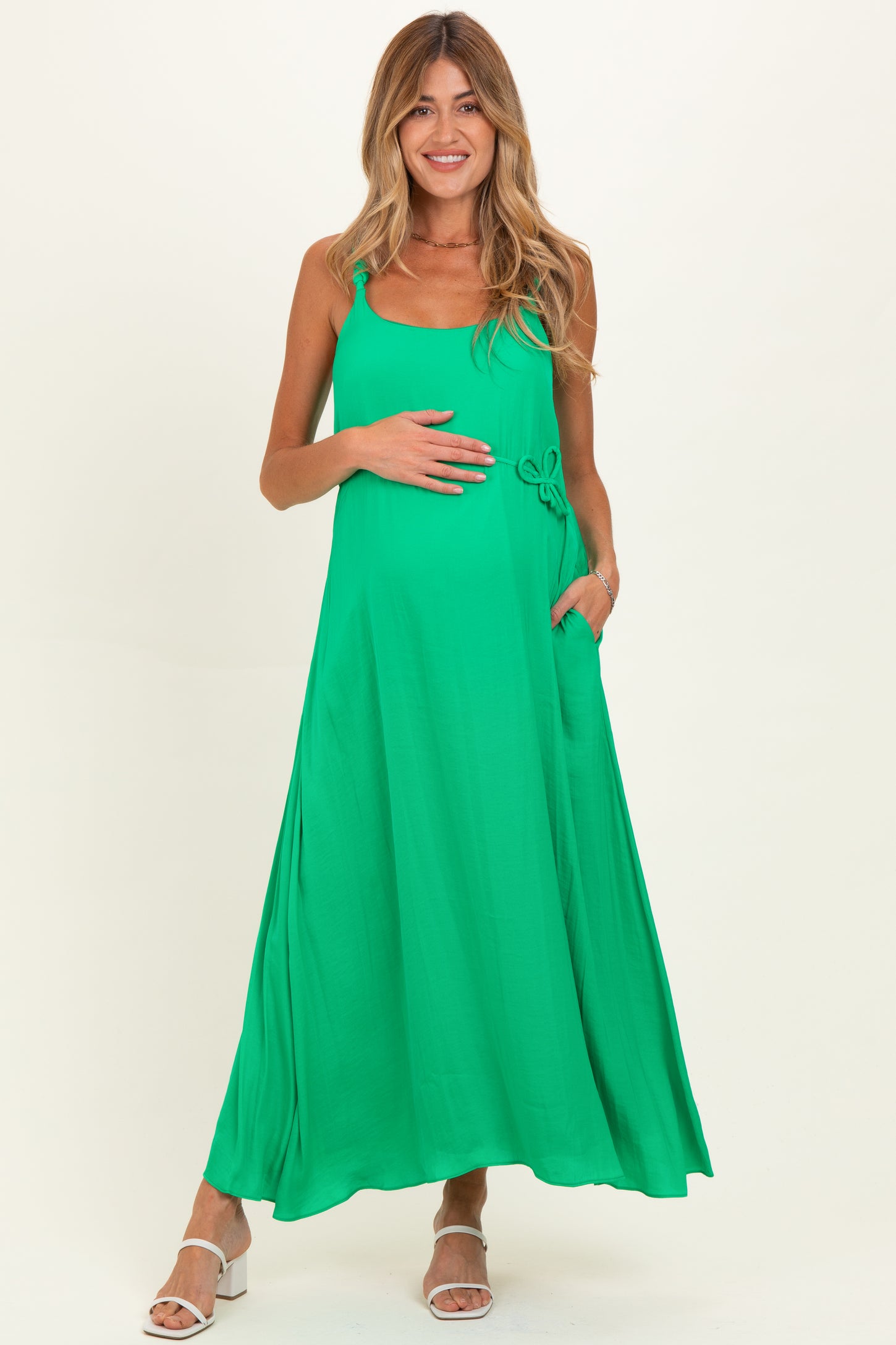 woman wearing a vibrant green maternity maxi dress with adjustable straps and side pockets, holding her baby bump