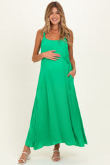 woman wearing a vibrant green maternity maxi dress with adjustable straps and side pockets, holding her baby bump