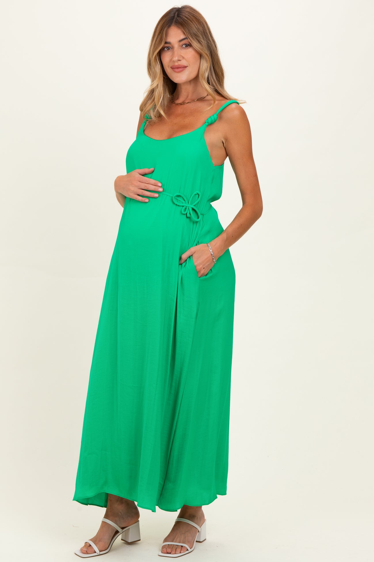 woman wearing a bright green maternity maxi dress with a bow detail, holding her baby bump
