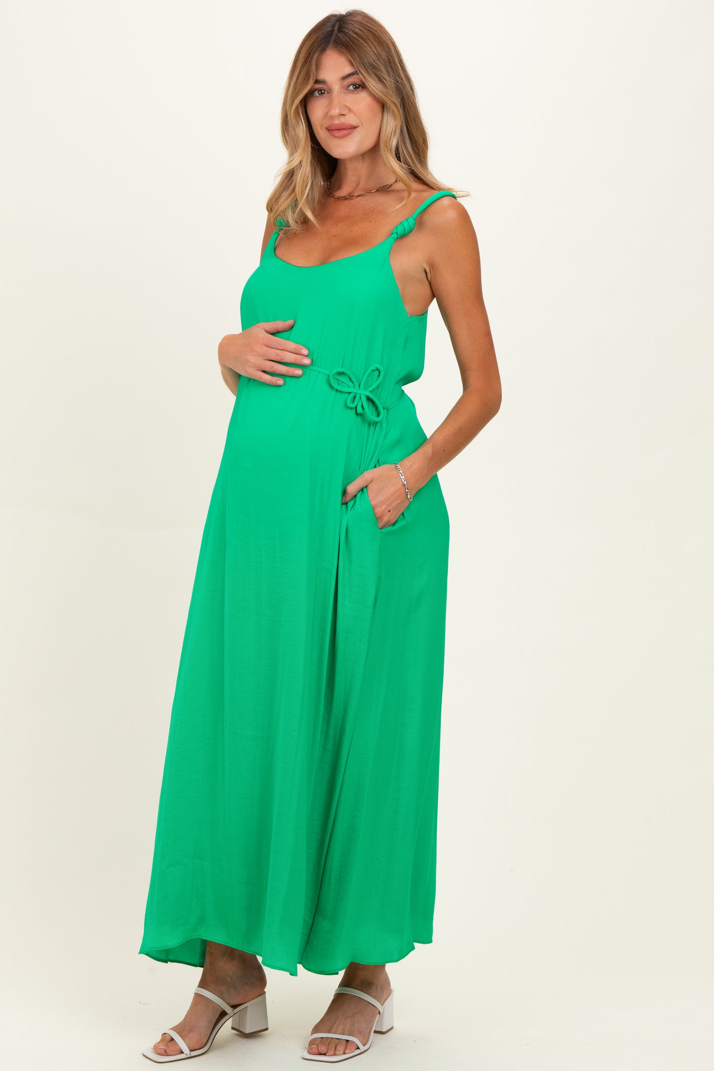 woman wearing a bright green maternity maxi dress with a bow detail, holding her baby bump