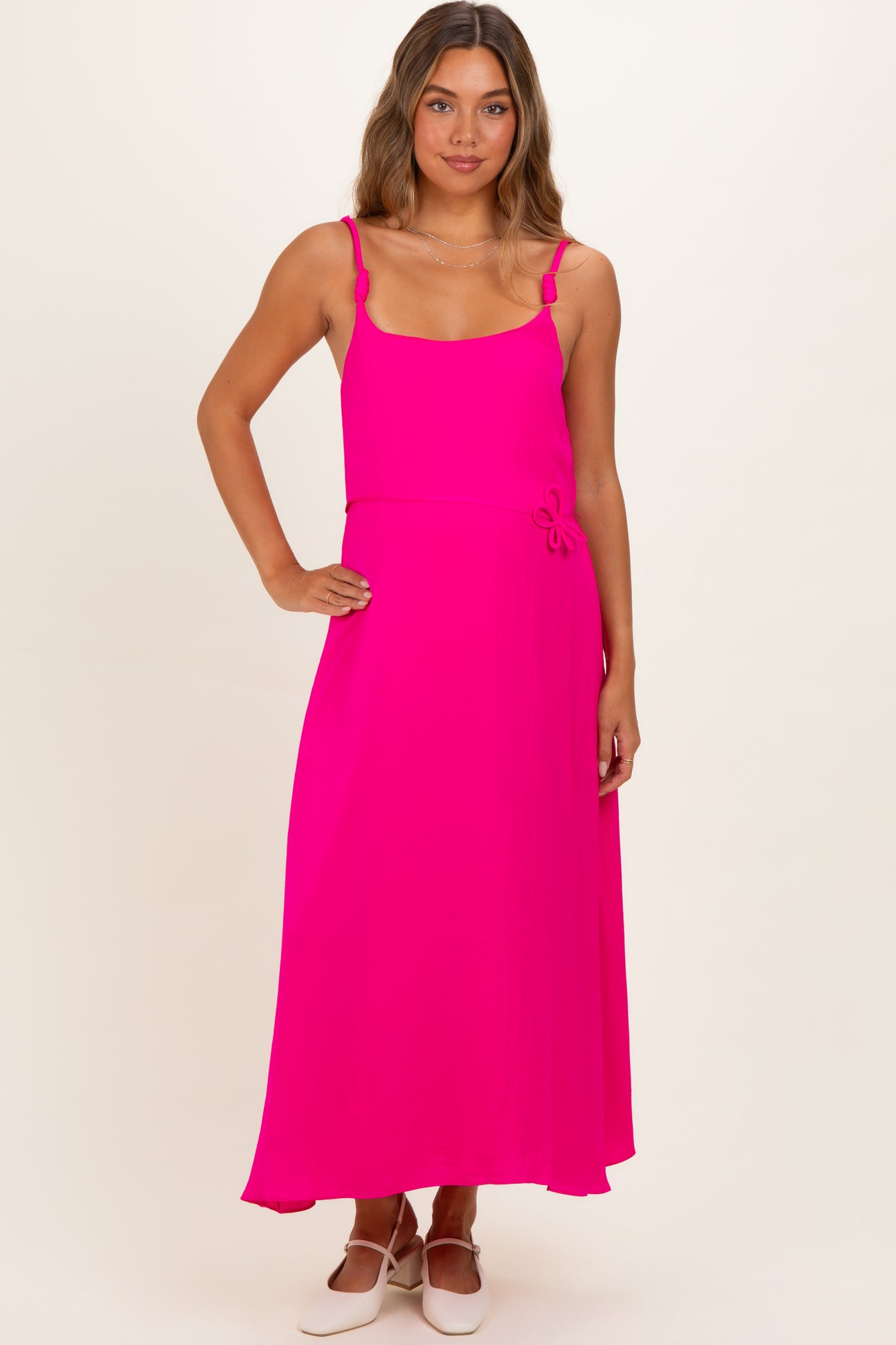 woman wearing a bright pink maternity maxi dress with adjustable straps and a floral accent detail on the waist