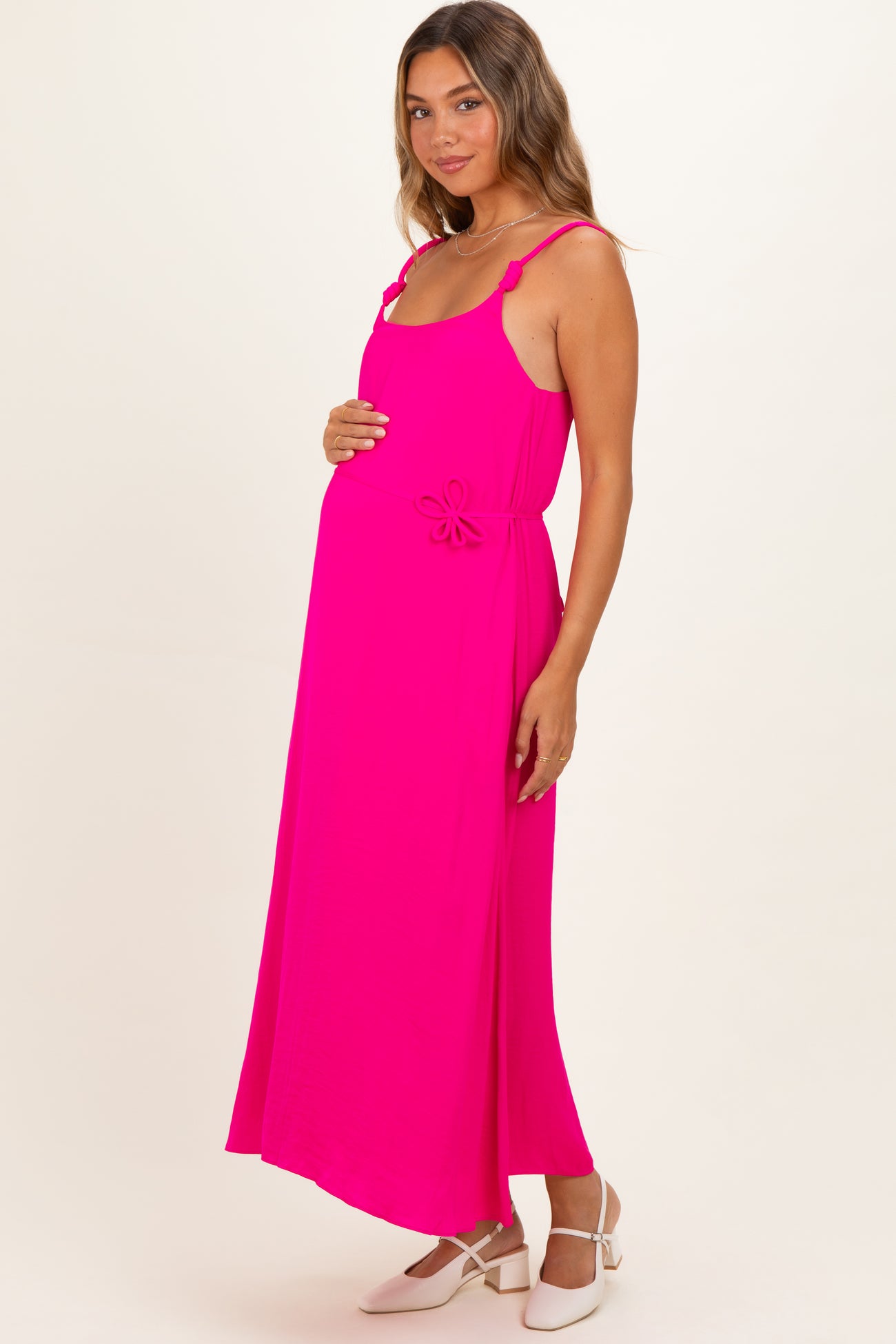 woman wearing a bright pink maternity dress with a tie detail at the waist and holding her baby bump