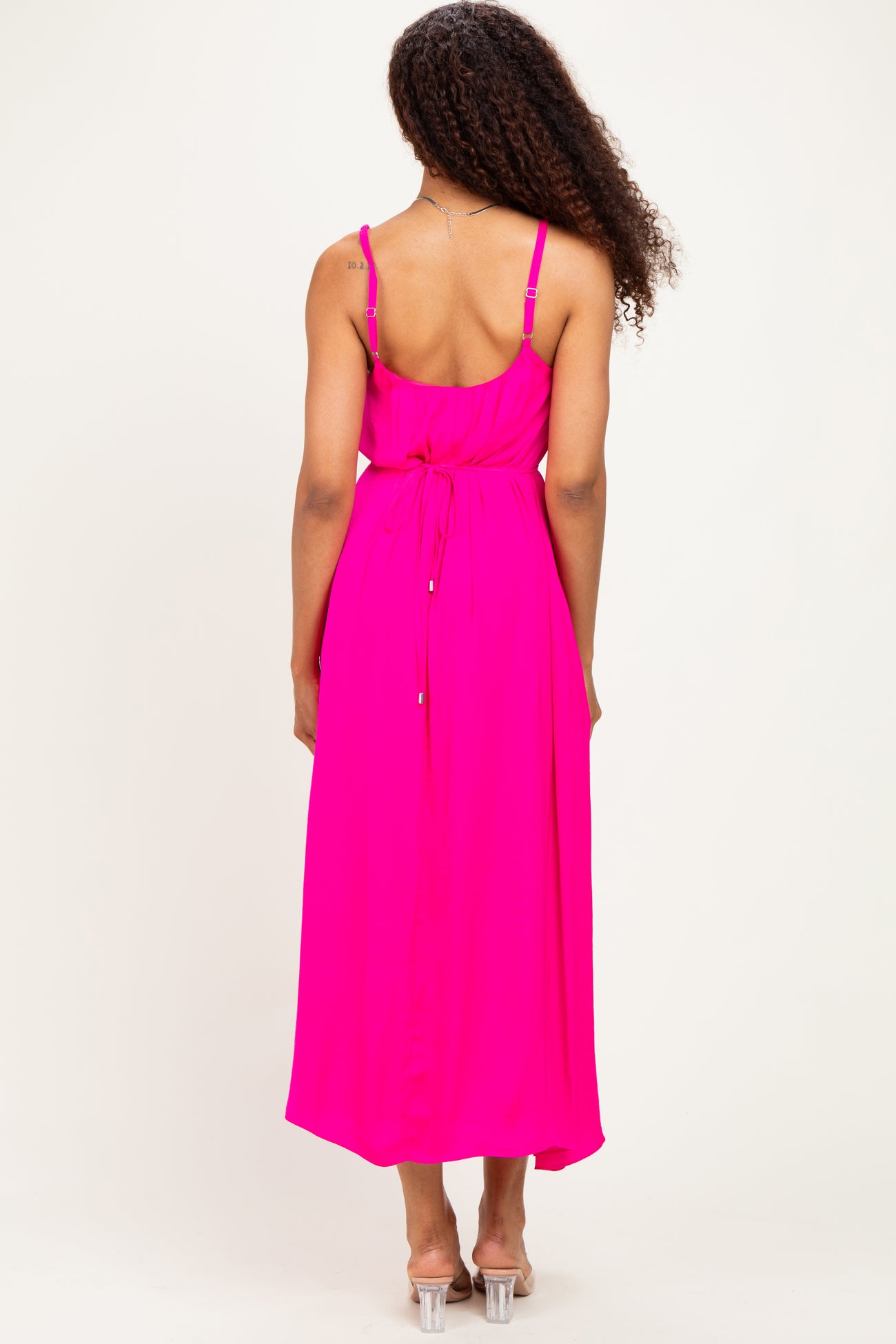 woman wearing a bright pink maxi dress with a tied waist and adjustable straps, viewed from the back