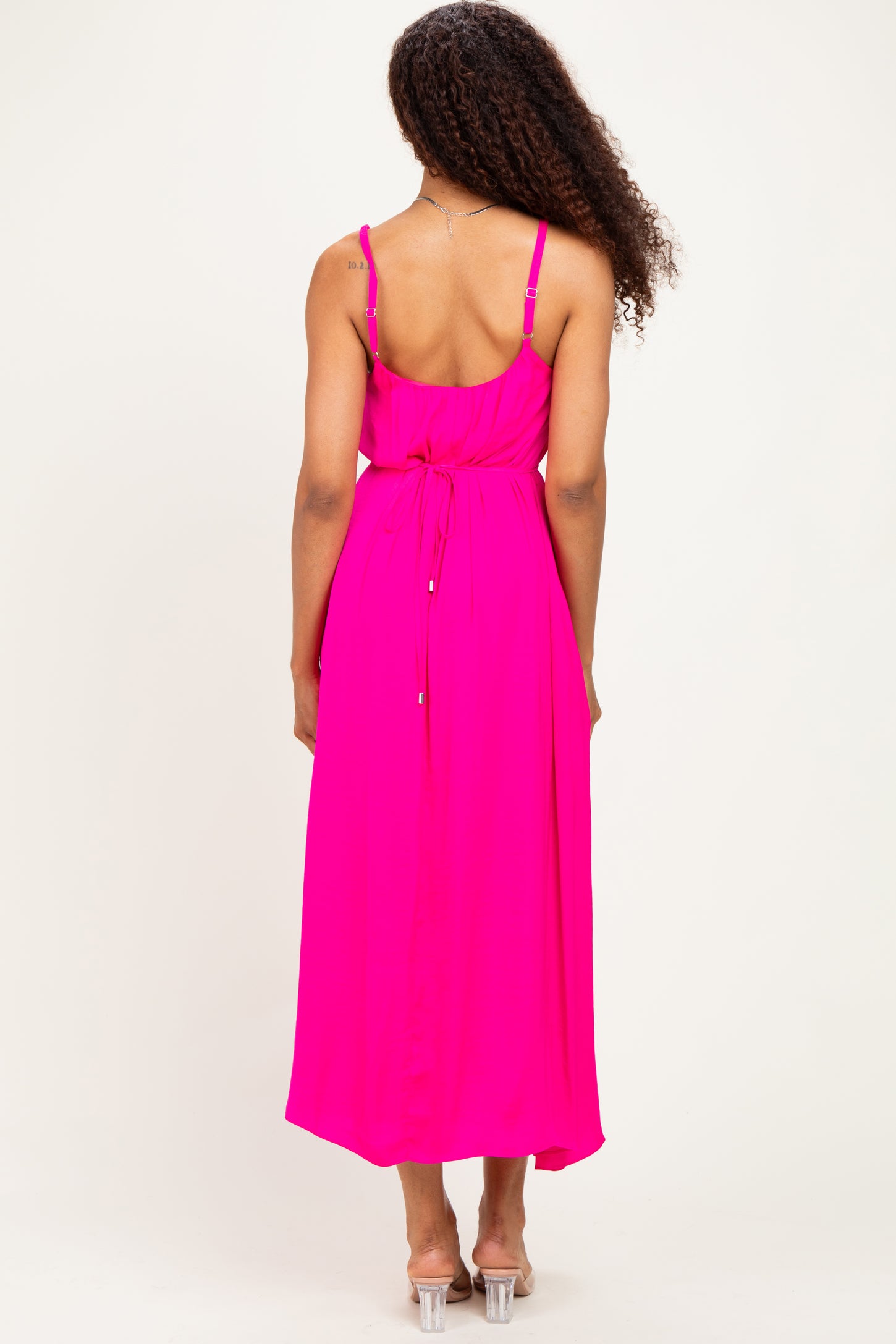 woman wearing a bright pink maxi dress with a tied waist and adjustable straps, viewed from the back