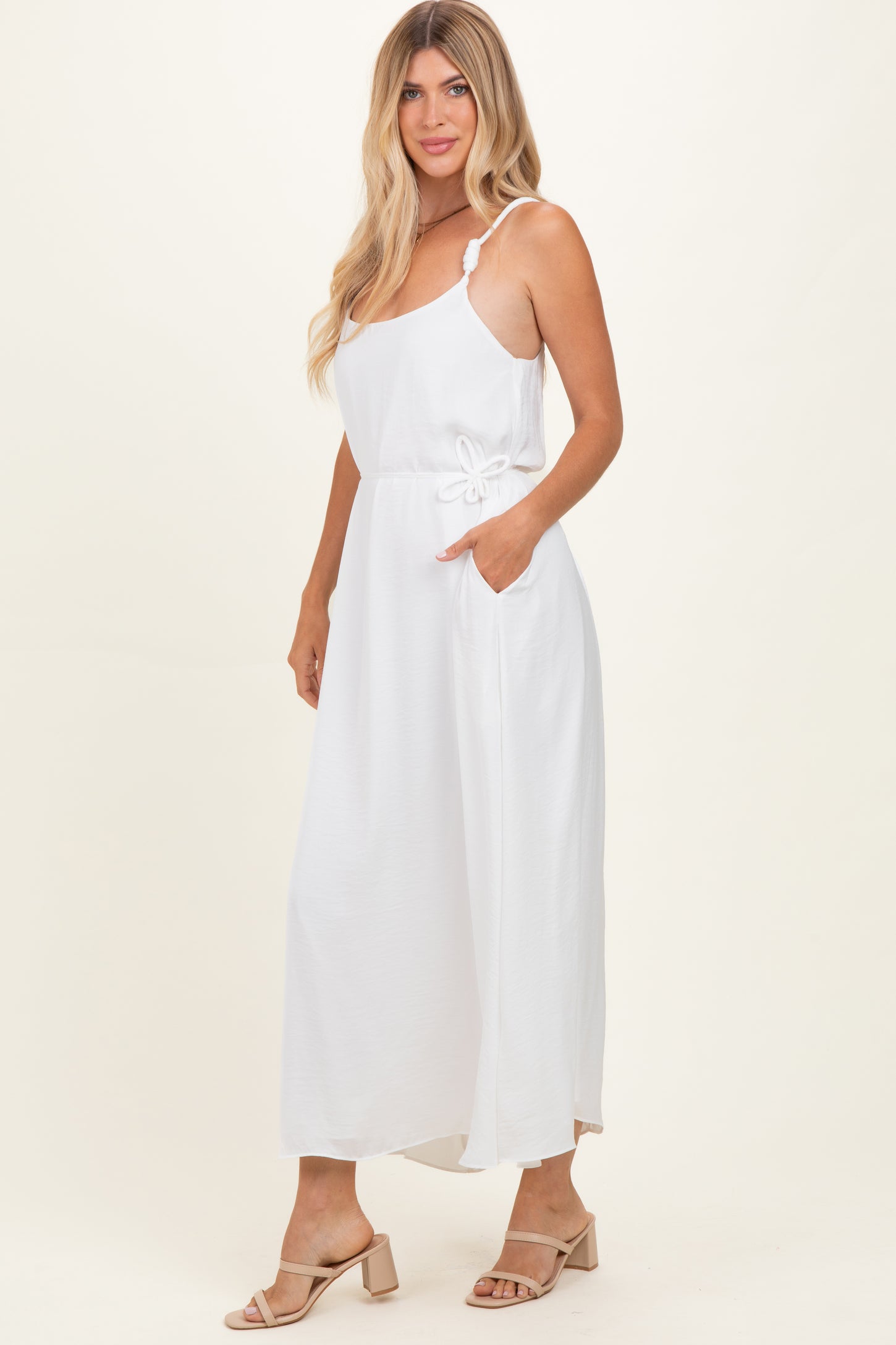 woman wearing a white maxi dress with spaghetti straps and a drawstring waist, standing with hands in pockets