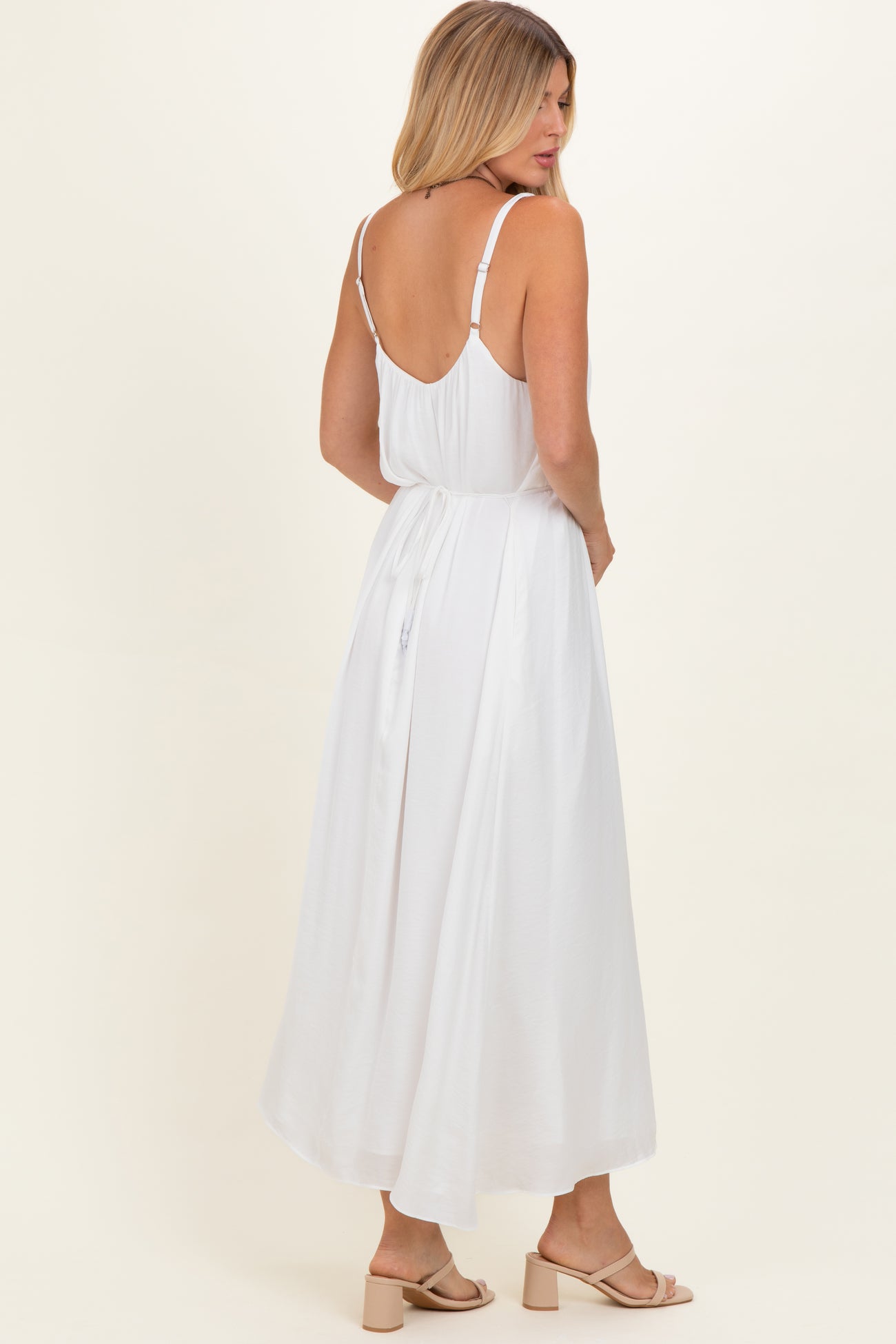 woman wearing a white maxi dress with thin straps and a tie-back detail, showing the back view