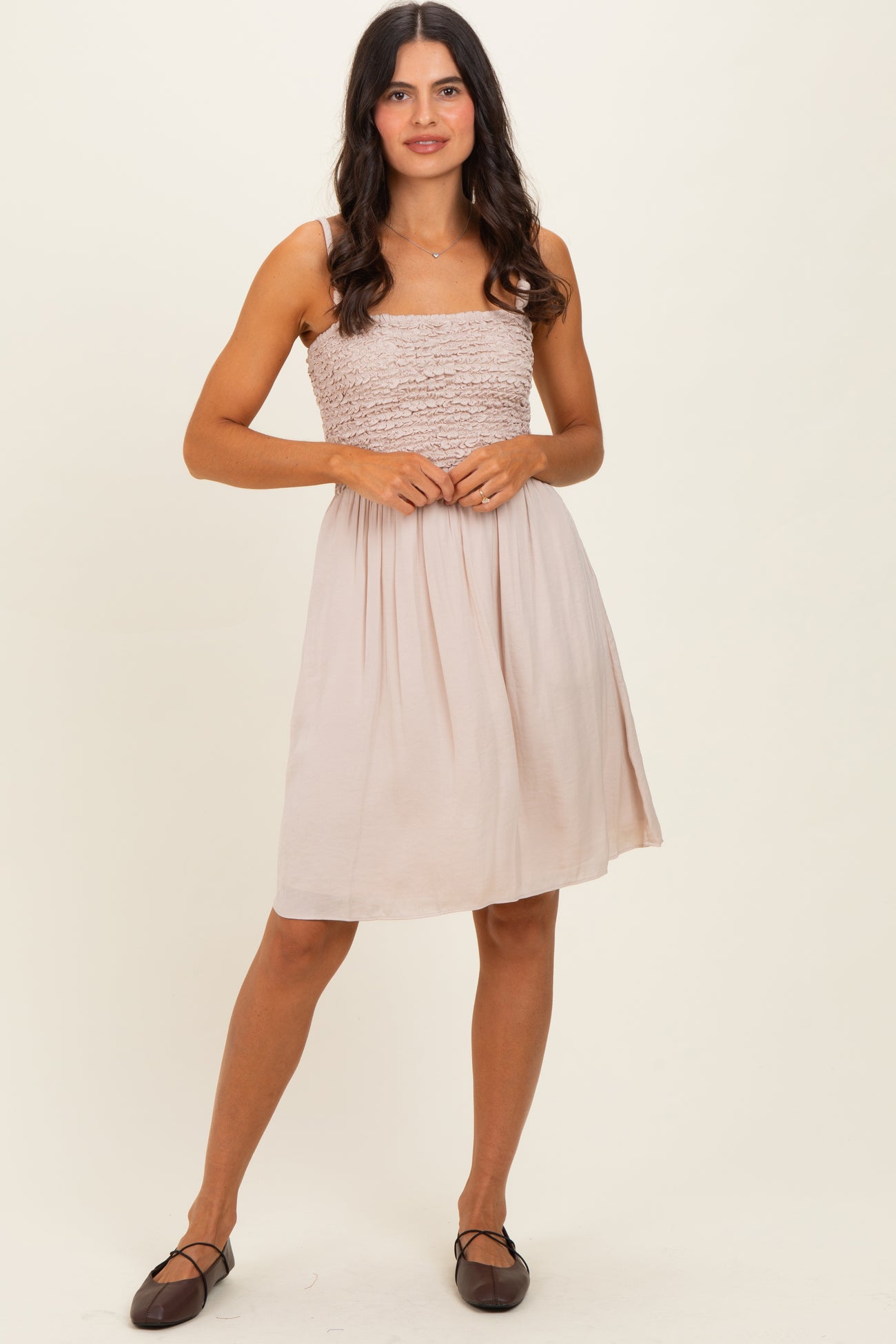woman wearing a light beige smocked sundress with a fitted bodice and a flared skirt, paired with brown flats