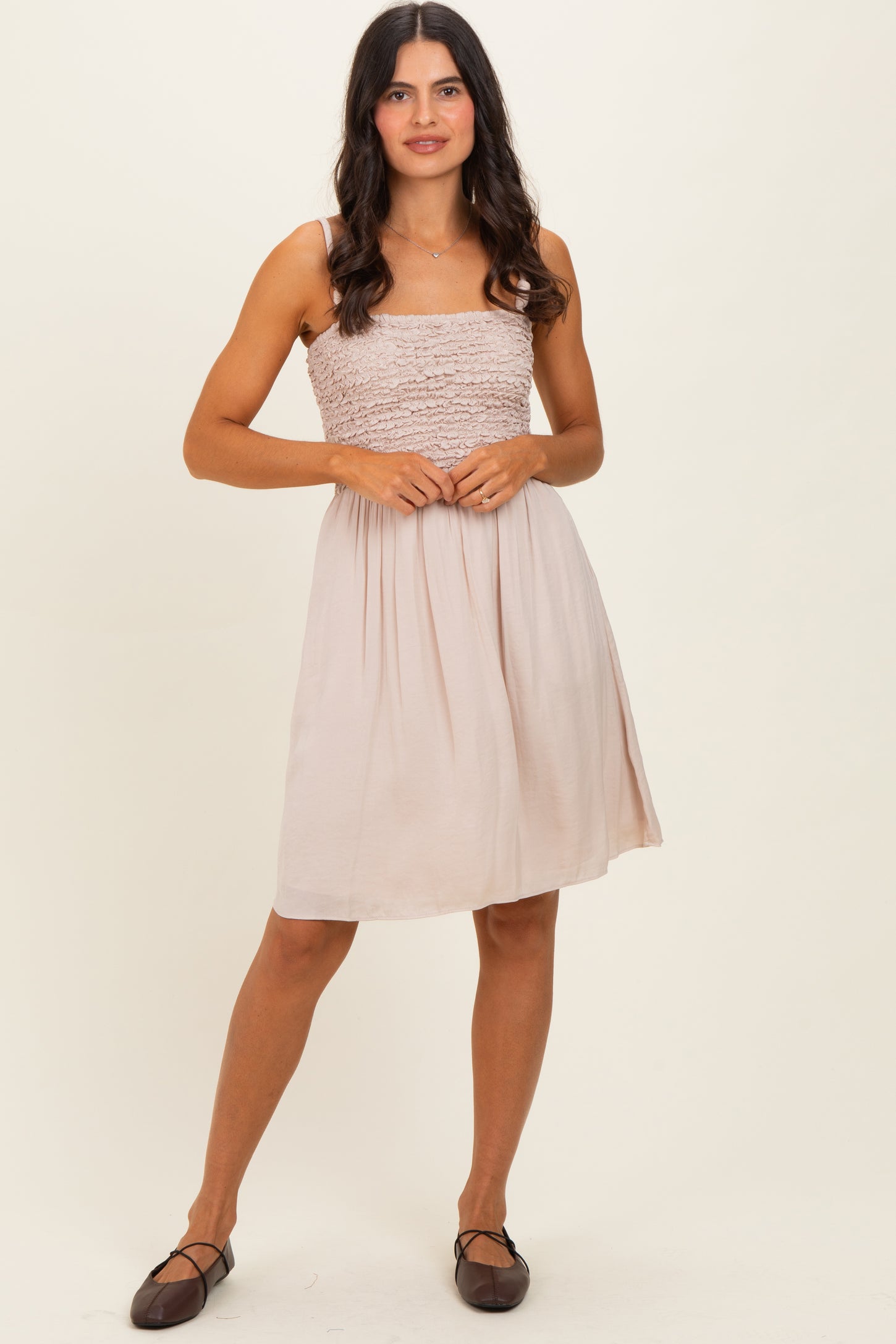 woman wearing a light beige smocked sundress with a fitted bodice and a flared skirt, paired with brown flats