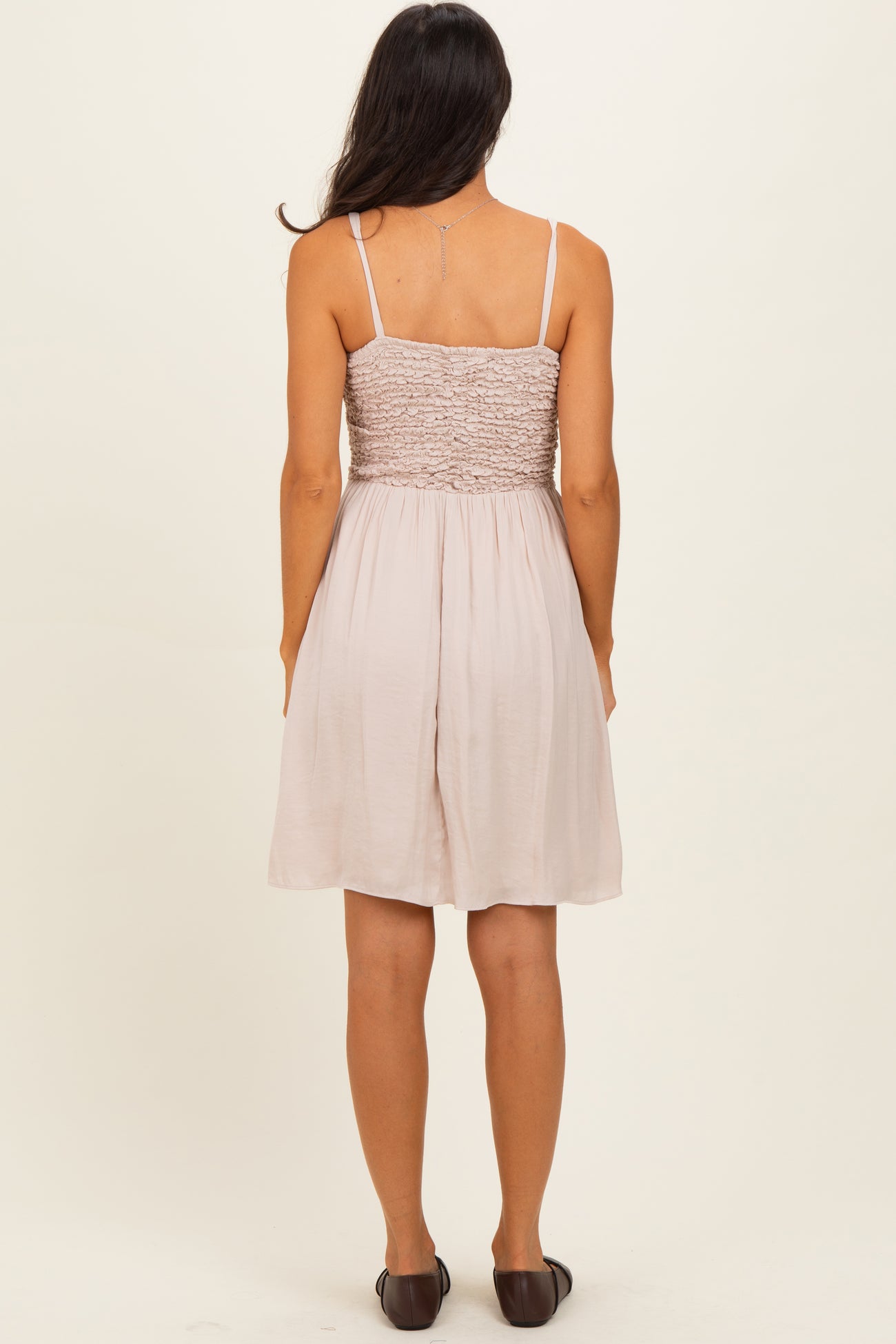 woman wearing a light pink smocked back sundress with thin straps, viewed from the back