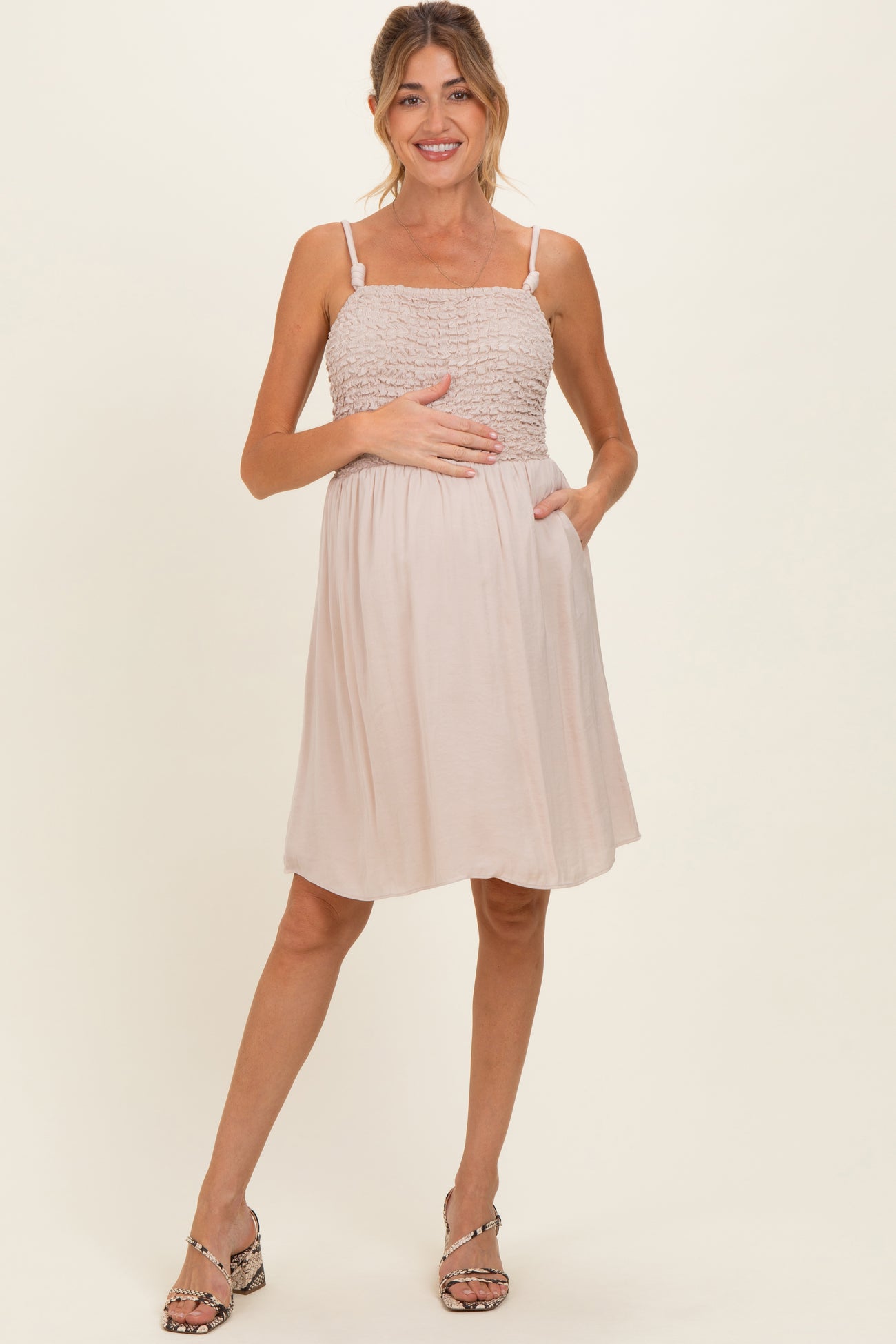 woman wearing a light pink maternity dress with smocked bodice and pockets, holding her baby bump