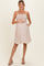 woman wearing a light pink maternity dress with smocked bodice and pockets, holding her baby bump