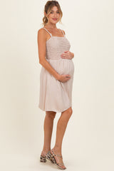 woman wearing a light beige maternity dress with a smocked bodice and flowing skirt, holding her baby bump