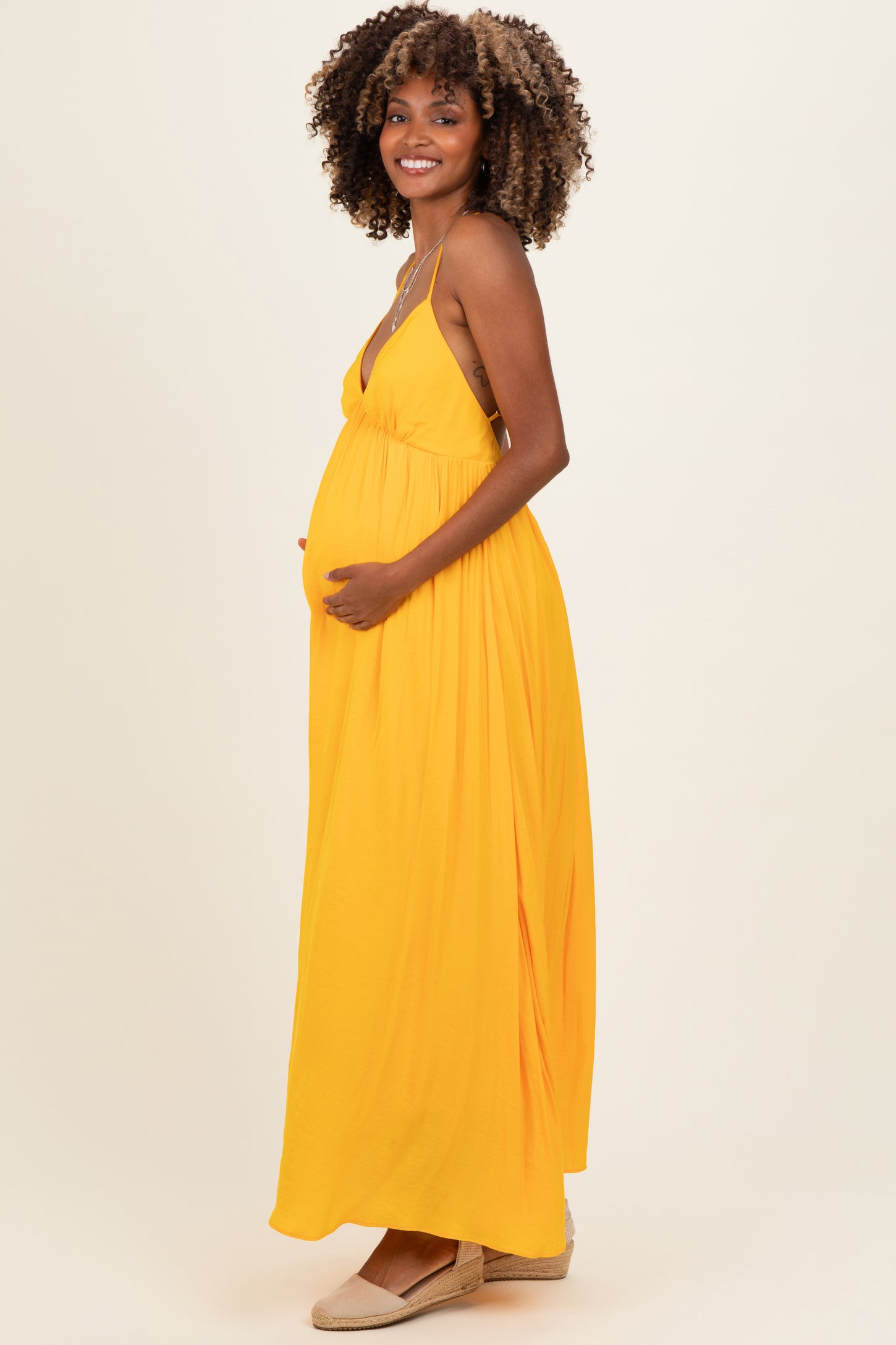 woman wearing a yellow maternity maxi dress, smiling and holding her baby bump