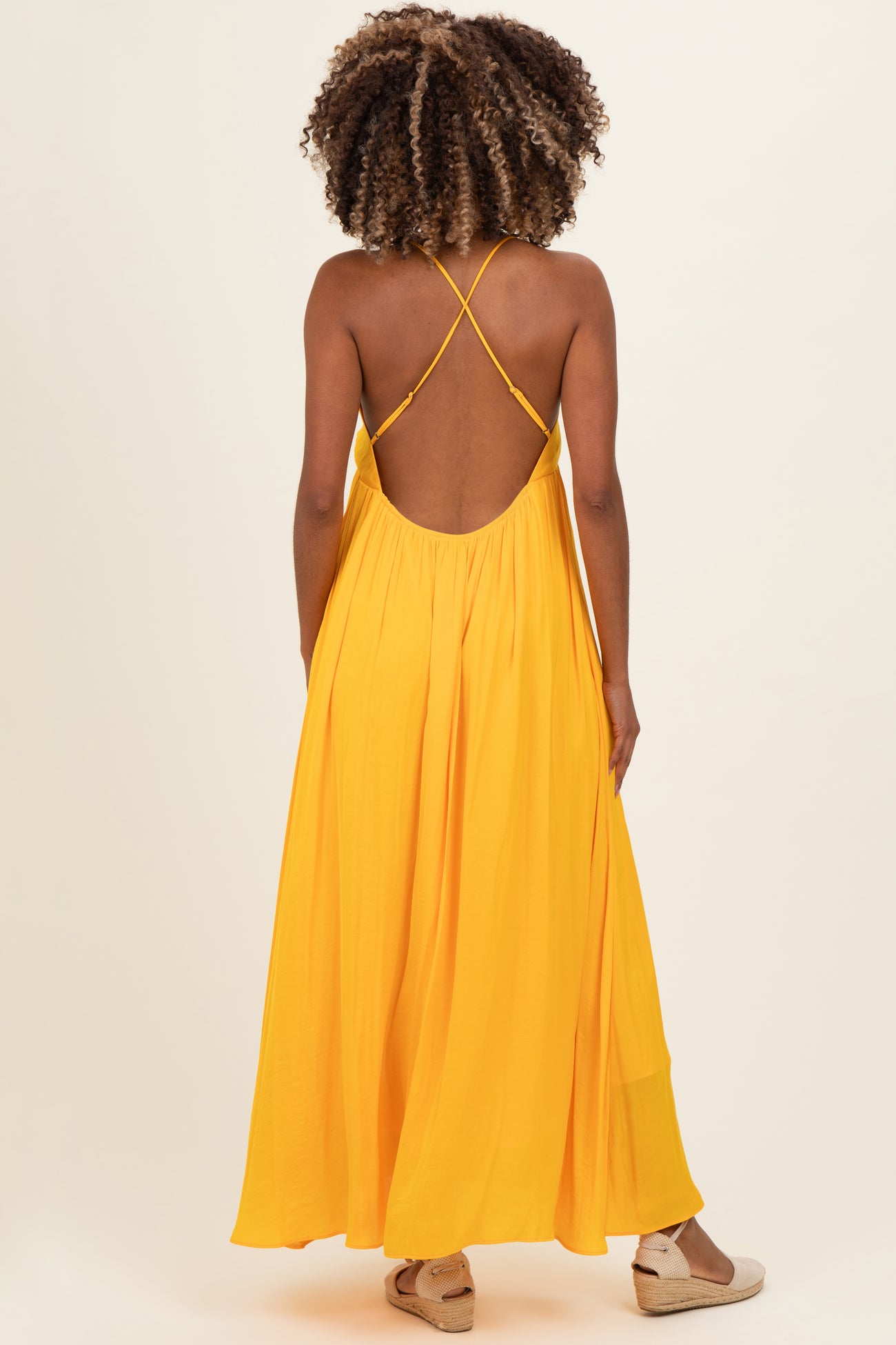woman wearing a bright yellow maternity maxi dress with crisscross straps and a flowy silhouette
