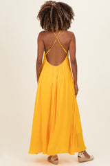 woman wearing a bright yellow maternity maxi dress with crisscross straps and a flowy silhouette