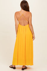 woman wearing a yellow backless maxi dress with crisscross straps and a flowy silhouette