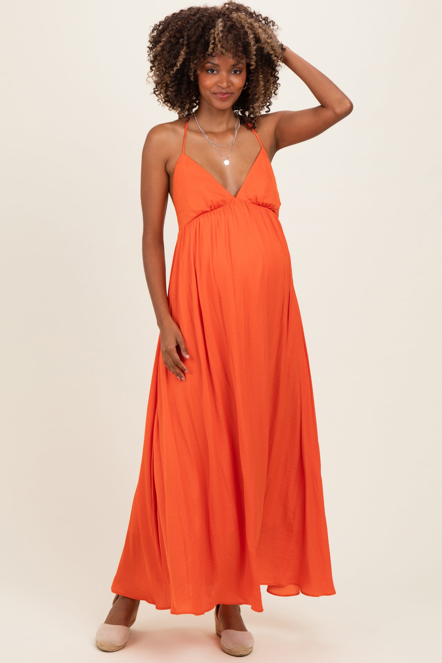 woman wearing a bright orange maternity maxi dress with a deep v-neckline and flowy skirt, showcasing her baby bump