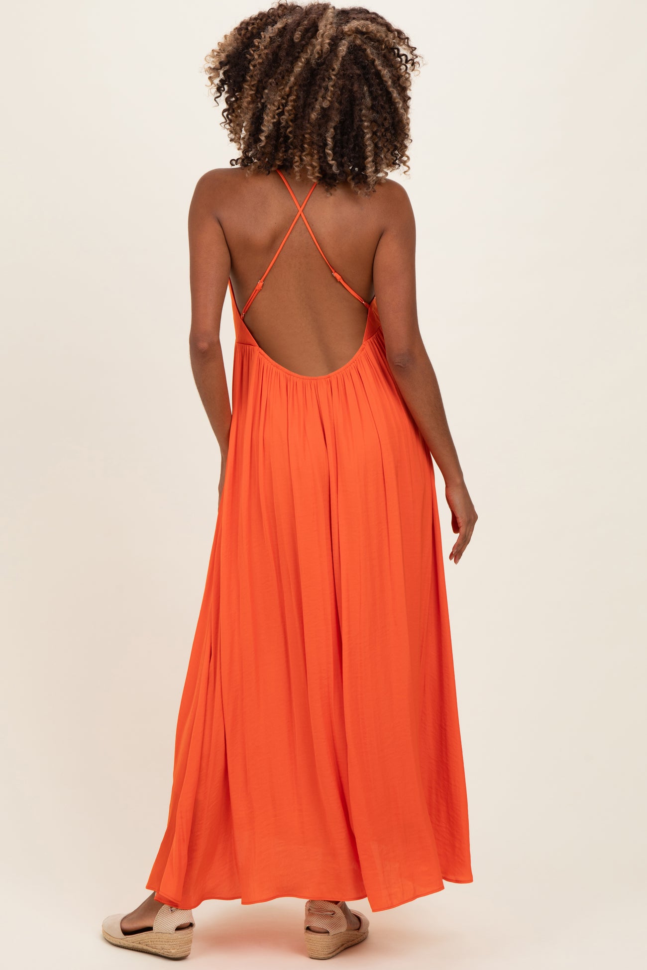 woman wearing an orange backless maternity maxi dress with crisscross straps and flowing silhouette