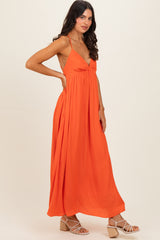 woman wearing an orange maxi dress with a deep neckline and spaghetti straps, styled with strappy sandals