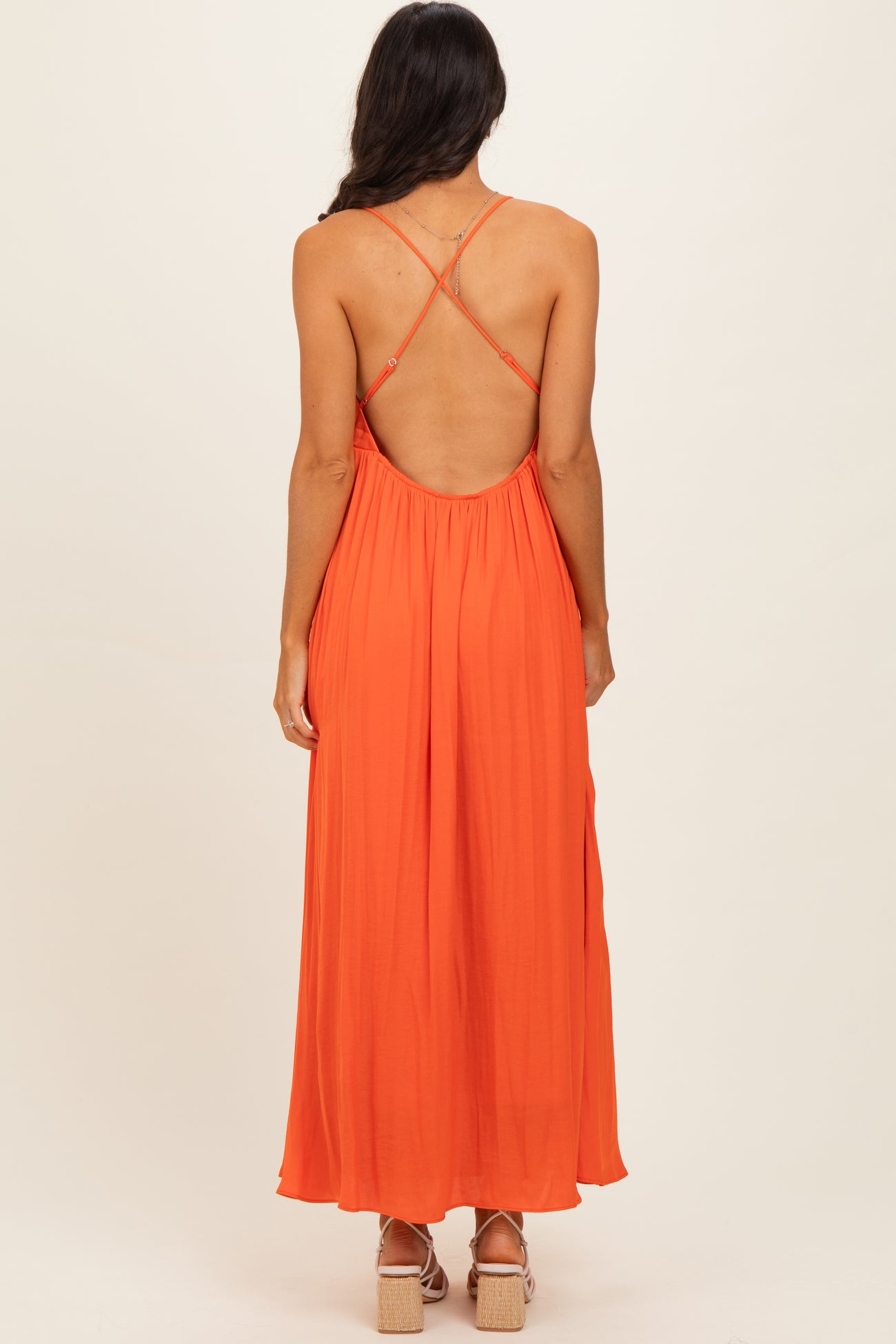 woman wearing a backless orange maxi dress with crisscross straps and flowing silhouette