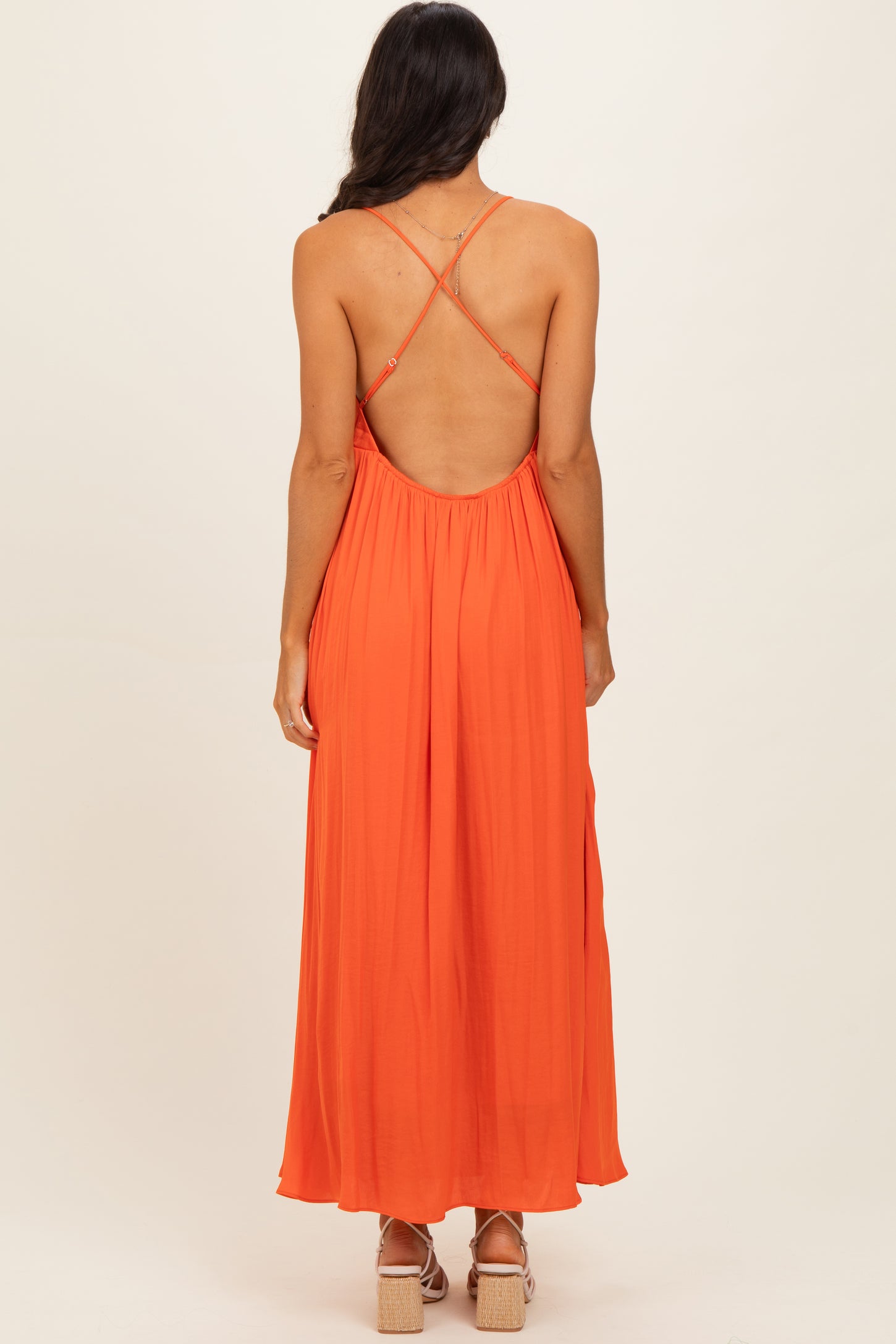 woman wearing a backless orange maxi dress with crisscross straps and flowing silhouette