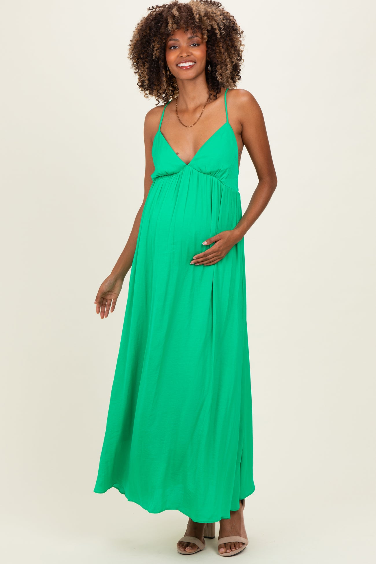 woman wearing a green sleeveless maternity maxi dress and holding her baby bump