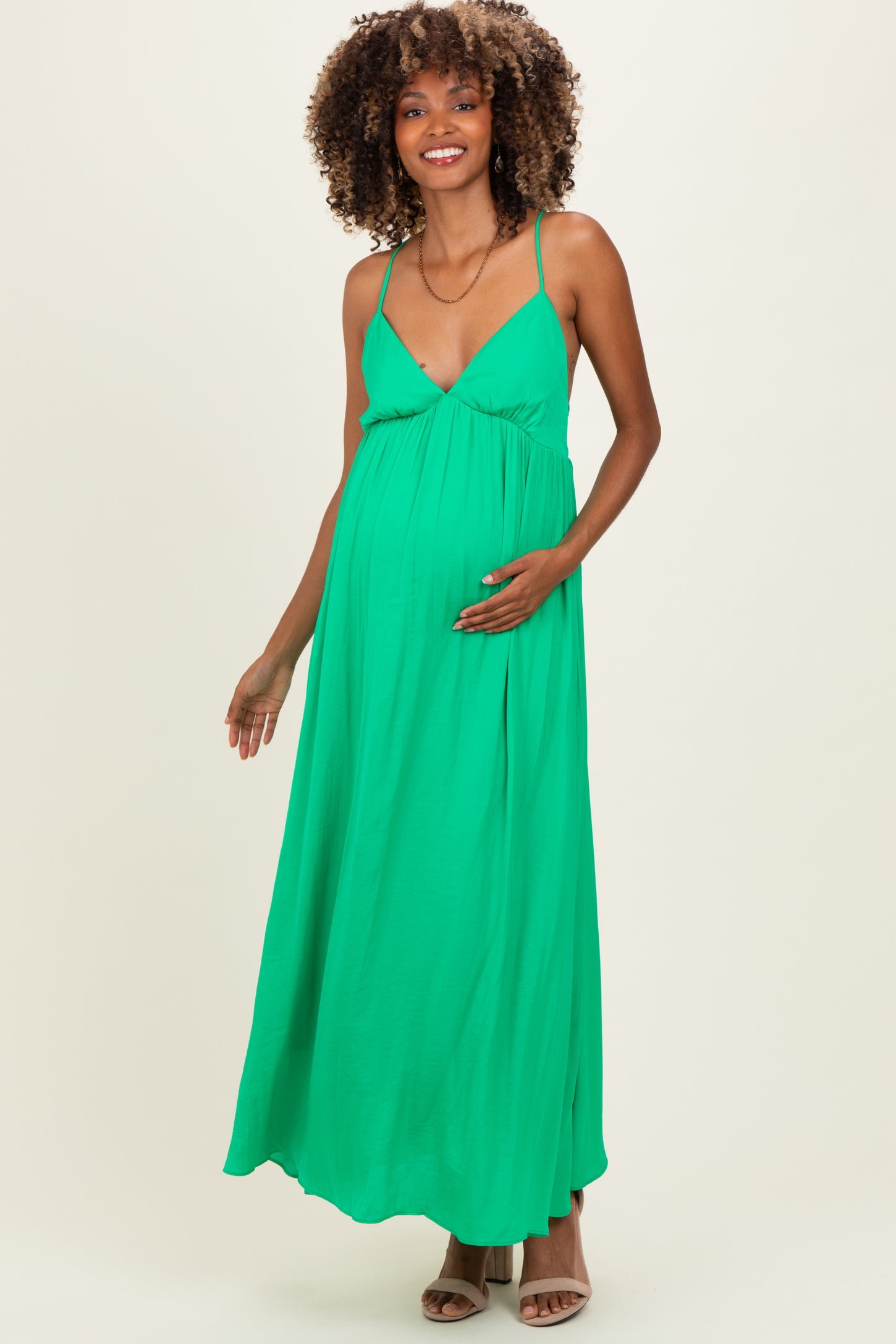 woman wearing a green sleeveless maternity maxi dress and holding her baby bump
